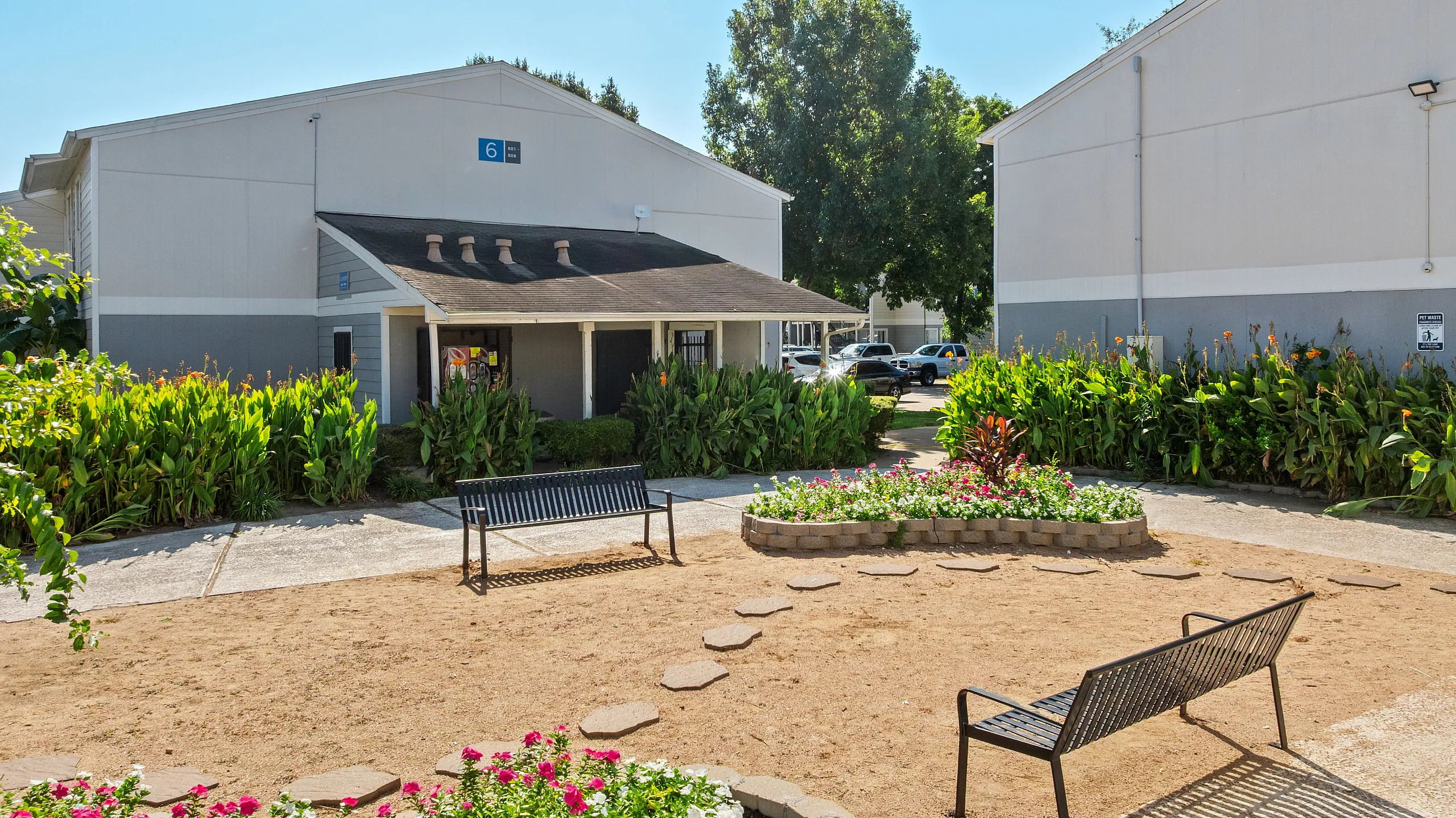Charming apartment complex with lush landscaping, inviting benches, and vibrant flowerbeds creating a serene outdoor ambiance.