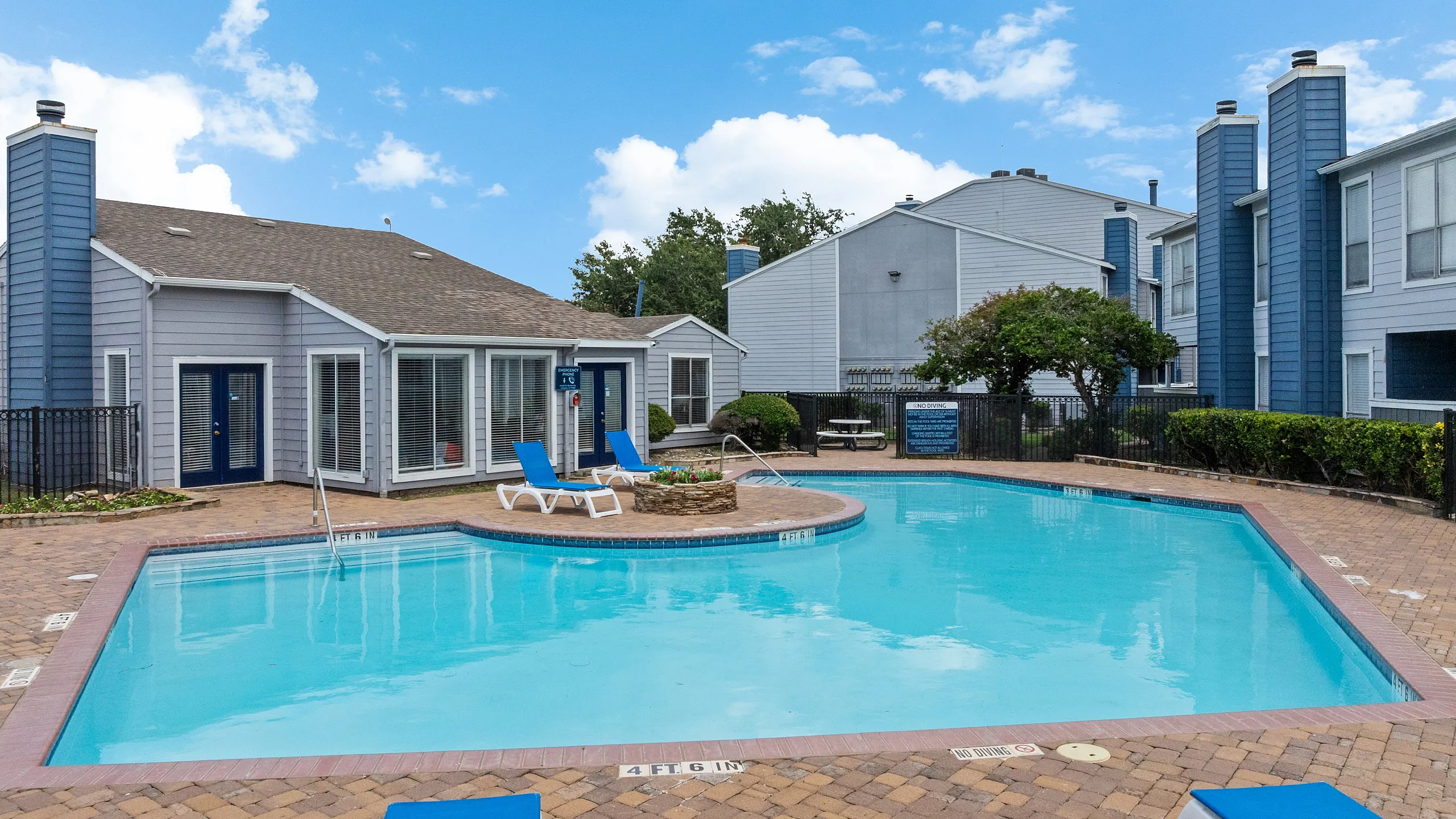 Charming apartment community featuring a sparkling blue swimming pool, elegant loungers, and modern architecture under a clear sky.