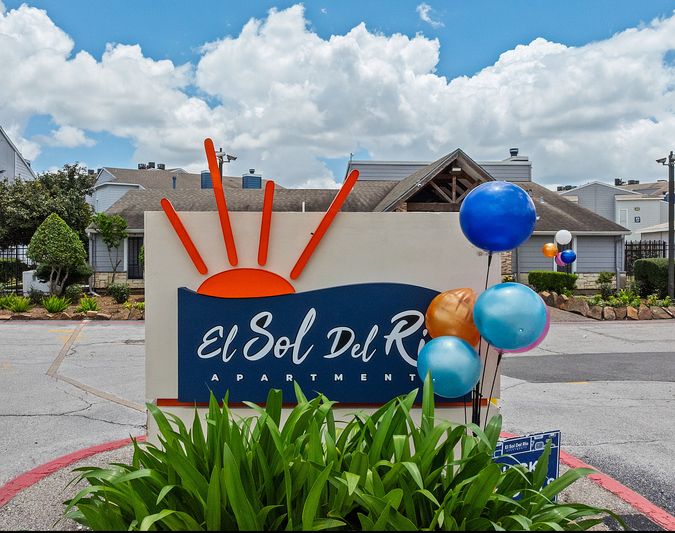 Welcoming entrance of El Sol Del Rio Apartments with vibrant balloons and lush greenery under a bright blue sky.