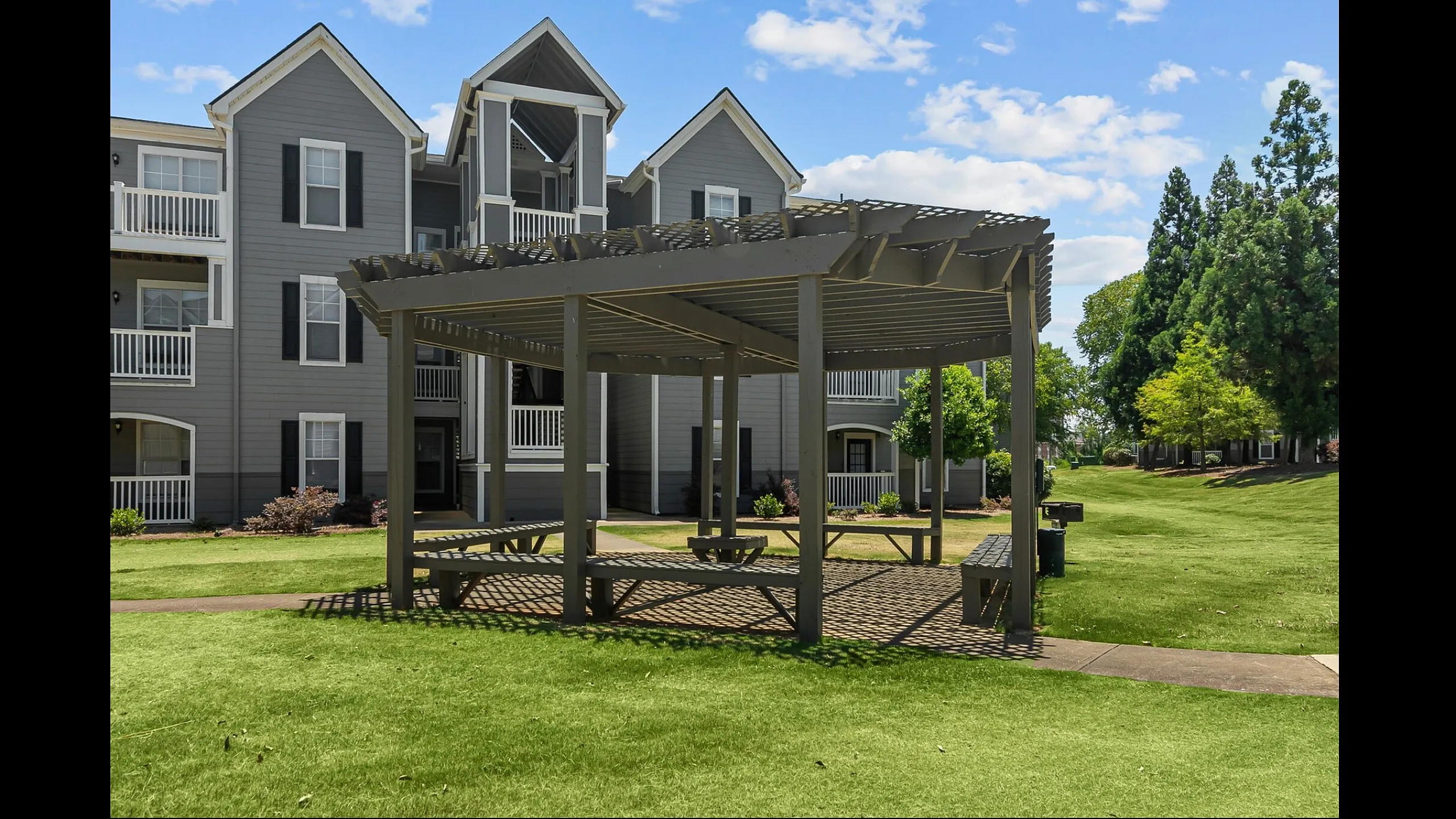 Charming apartment complex with elegant architecture, featuring a spacious pergola and vibrant green lawn, ideal for outdoor gatherings.