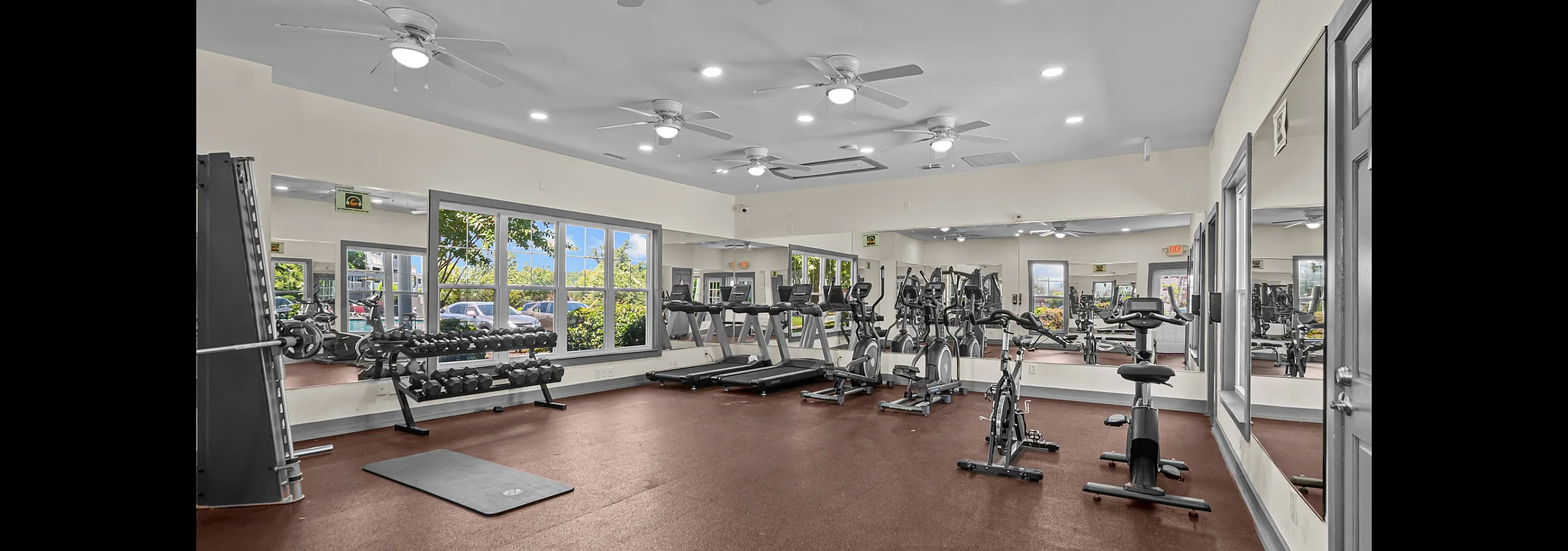 Bright and airy gym with modern fitness equipment, large mirrors, and natural light streaming through big windows.