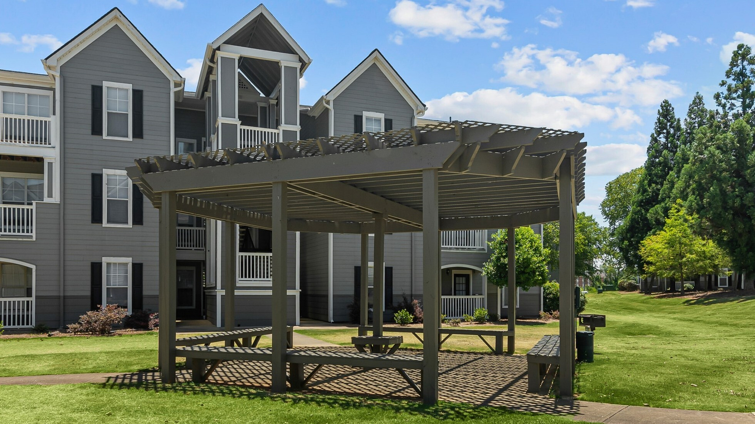 Charming apartment complex with modern architecture, surrounded by lush green lawns and featuring a stylish outdoor gazebo for relaxation.