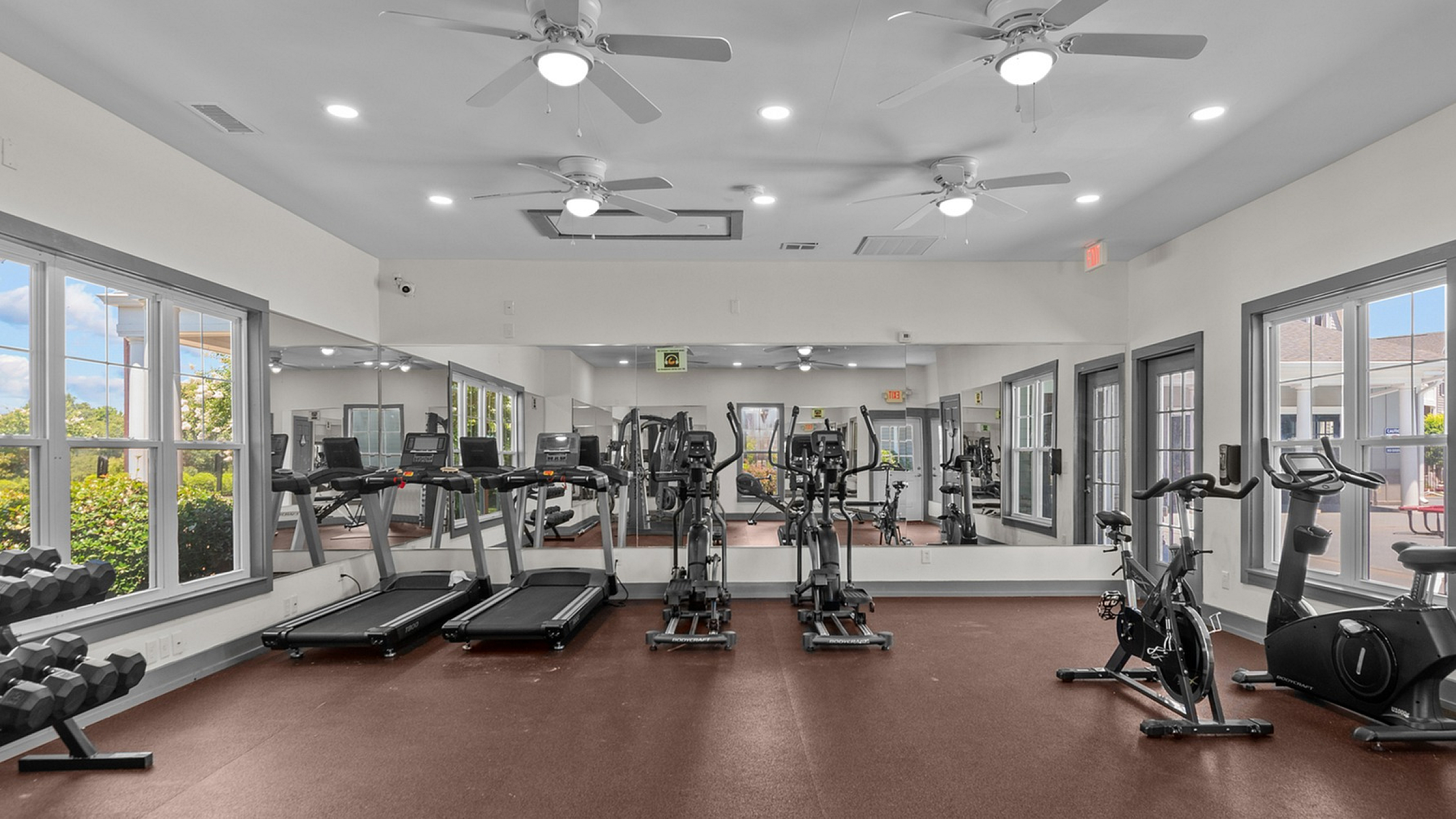 Modern fitness center with state-of-the-art treadmills, elliptical machines, and free weights, surrounded by large windows and mirrors for a refreshing workout experience.