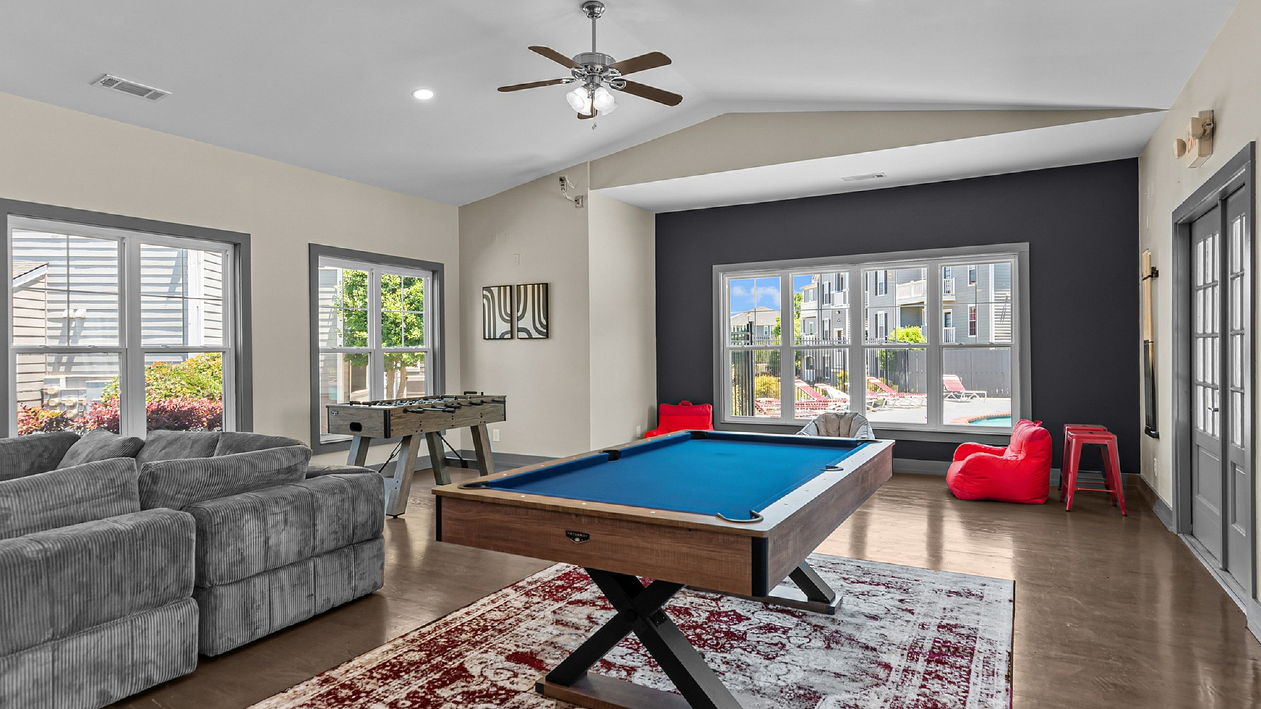 Vibrant recreation room featuring a sleek pool table, cozy couches, and large windows with a stunning pool view.