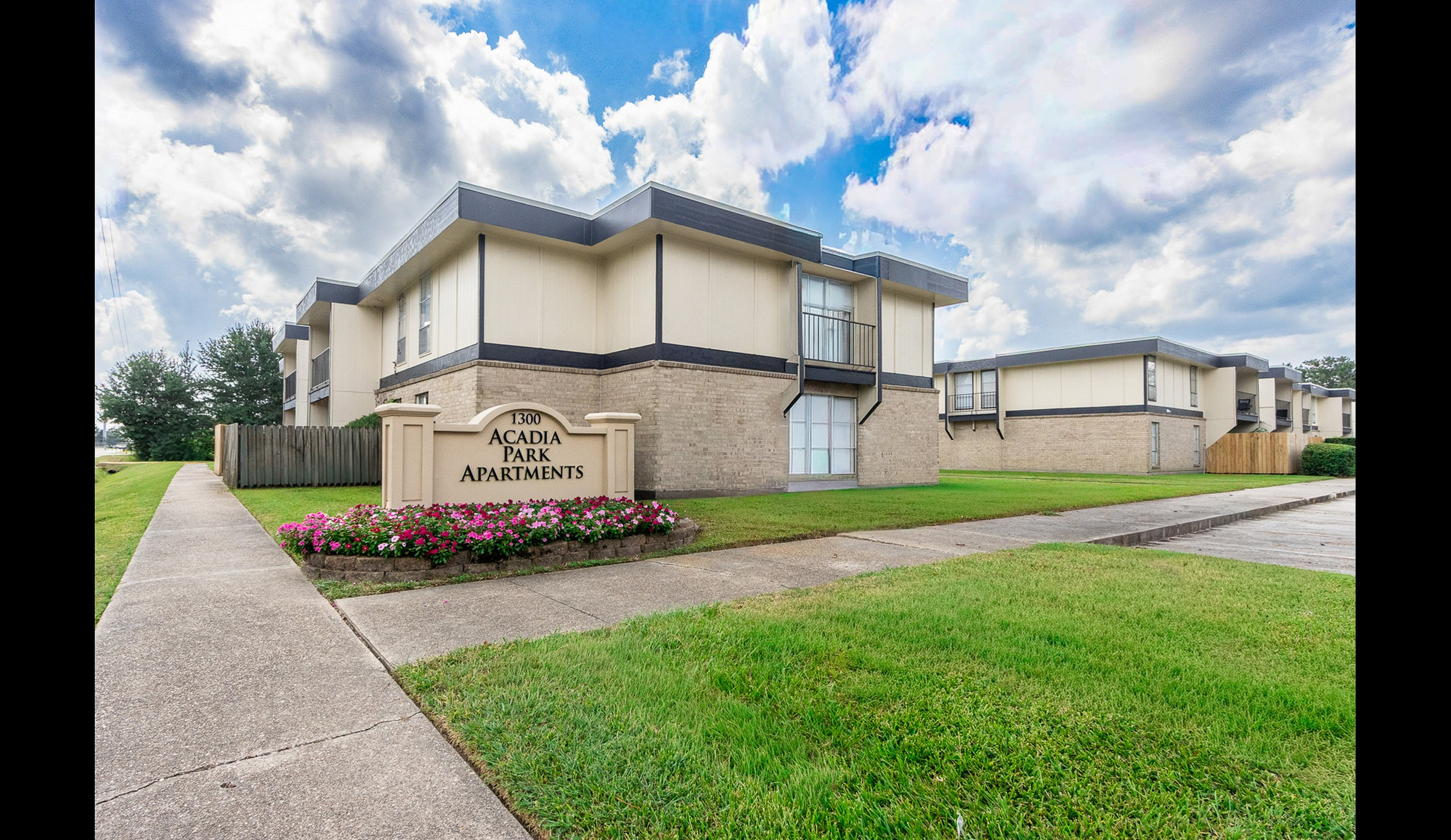 Charming Acadia Park Apartments with manicured lawns, stylish architecture, and vibrant flowers under a bright blue sky.