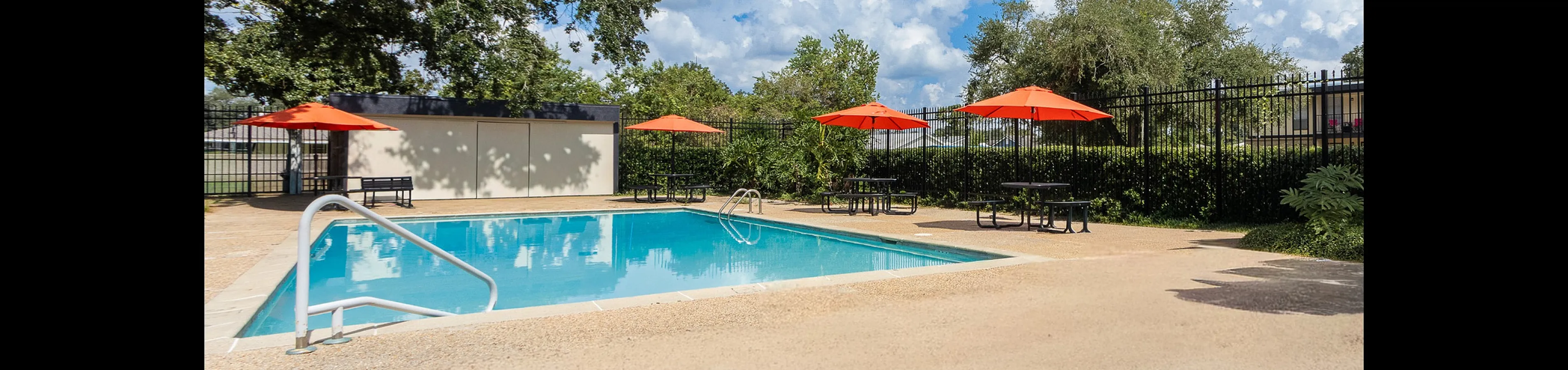 Inviting outdoor pool area with vibrant orange umbrellas, surrounded by lush greenery and blue skies.