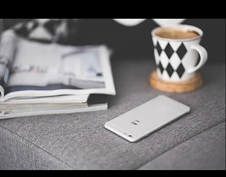 Cozy living room corner with a sleek smartphone, stylish magazine, and a chic patterned mug on a comfortable gray sofa.