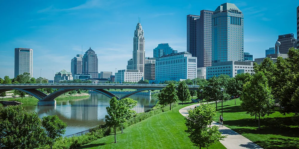 Vibrant cityscape with a modern skyline and scenic riverside park offering lush greenery and inviting walking paths.