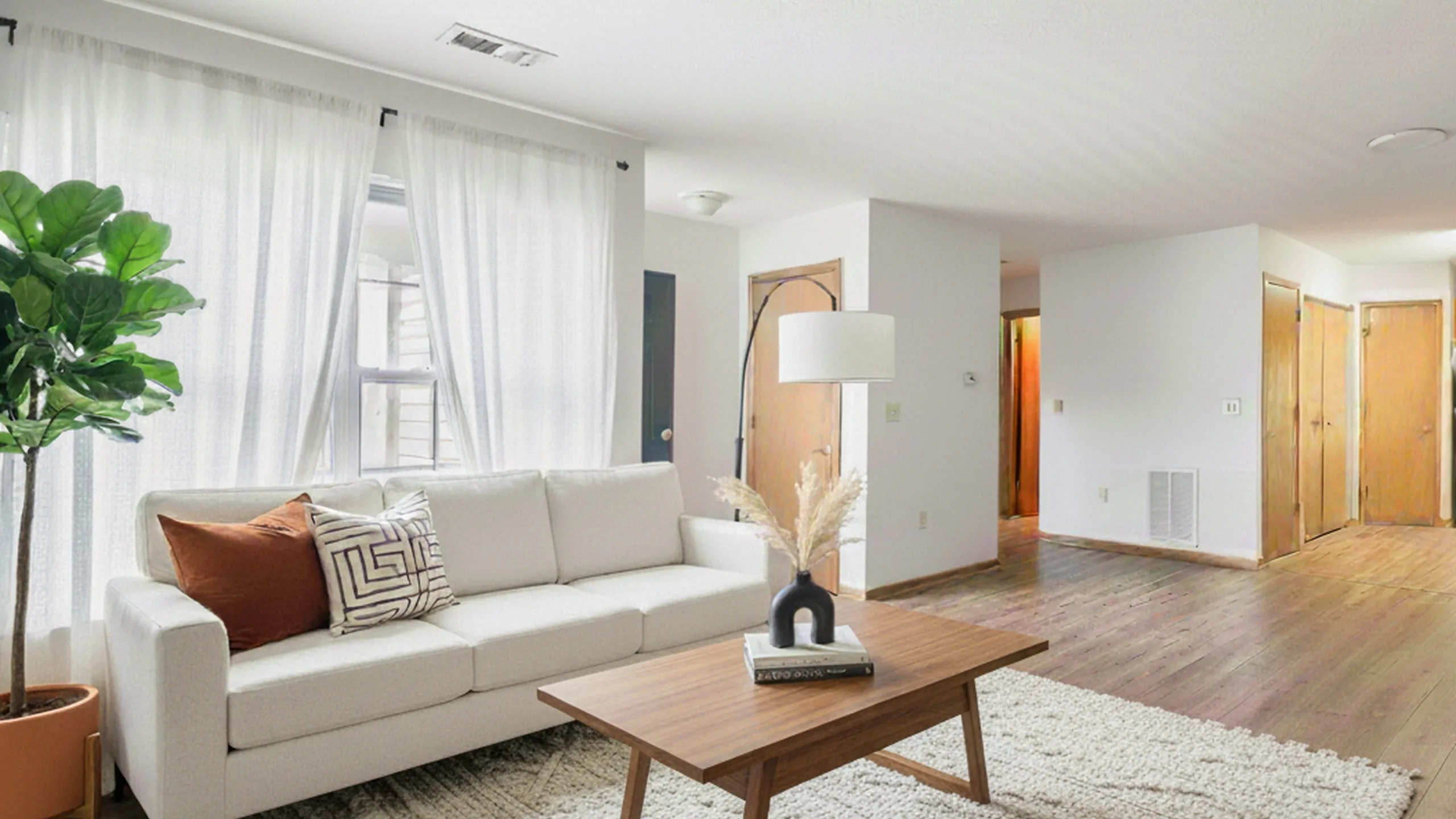 Bright and welcoming living room with a chic white sofa, stylish coffee table, elegant floor lamp, and lush green plant, creating a cozy and inviting atmosphere.