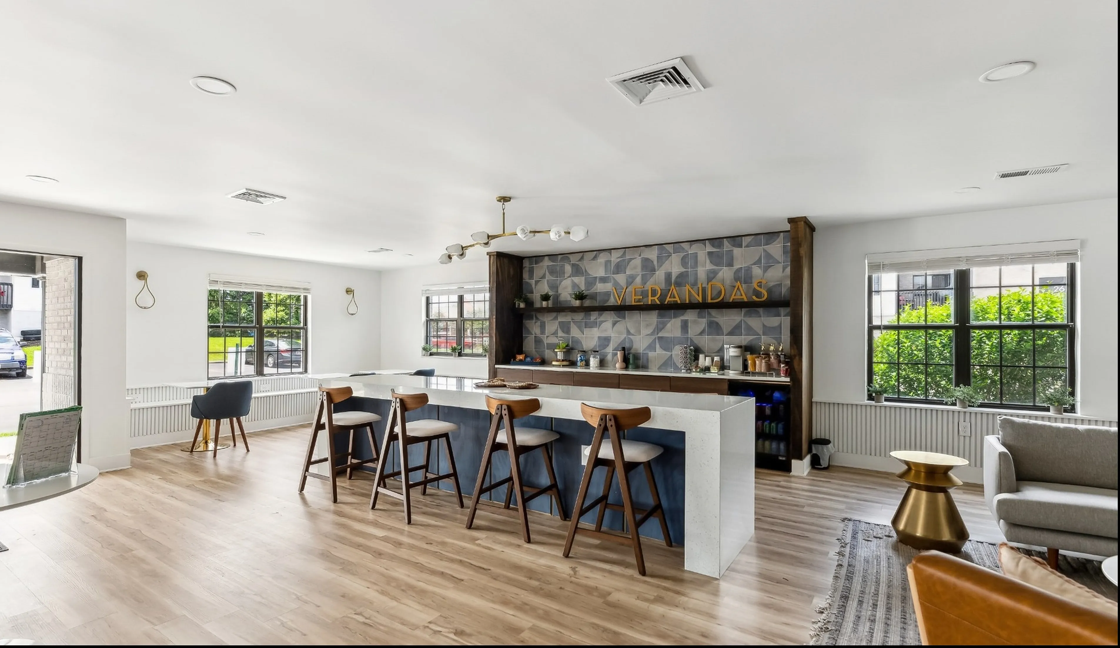 Bright and modern lounge featuring stylish bar seating, elegant decor, and large windows with lush greenery views.