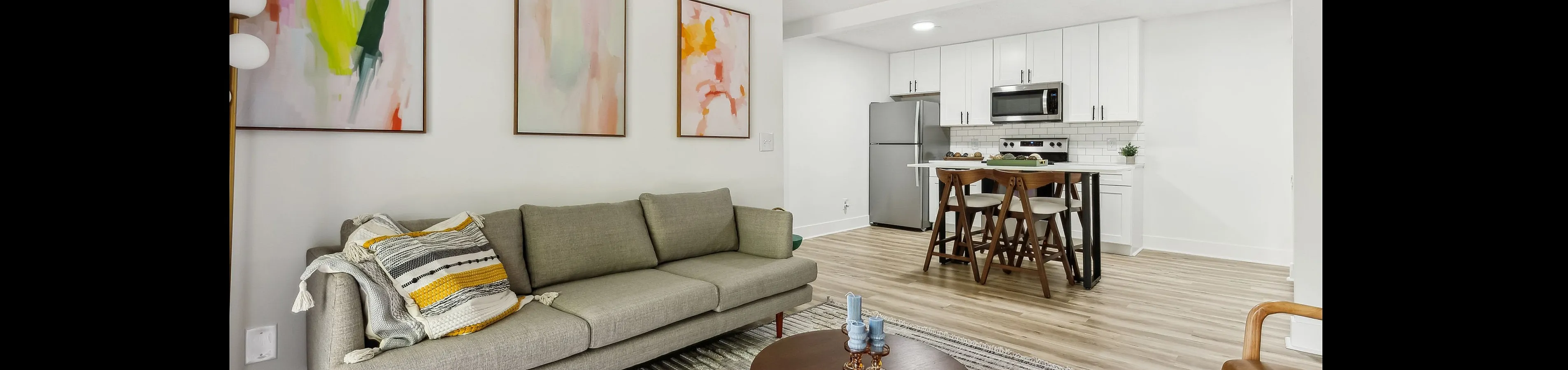 Chic open-plan living area featuring a modern kitchen, cozy gray sofa, and vibrant abstract artwork.