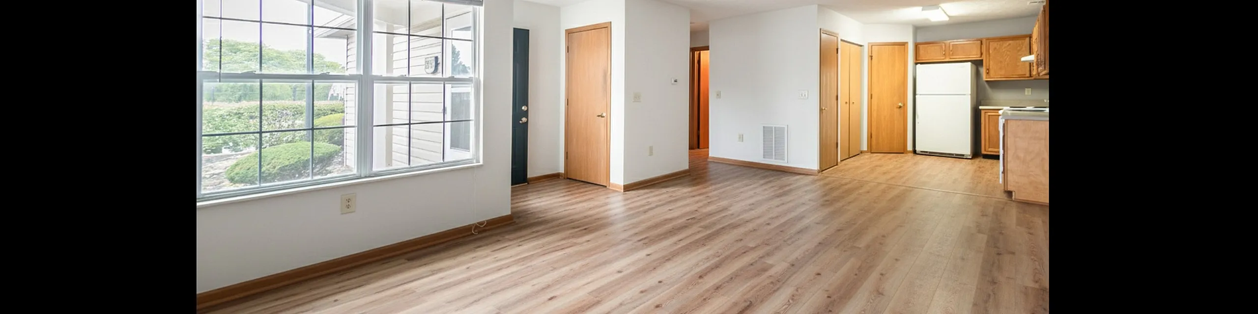 Bright and airy living space with large windows, modern wood flooring, and an open kitchen area with oak cabinets.