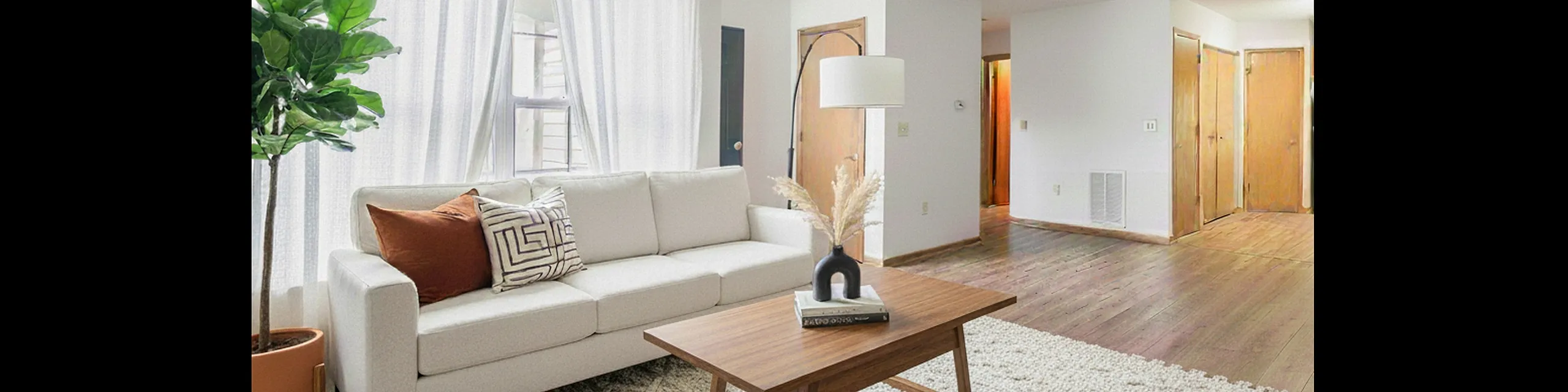 Bright, modern living room with a plush white sofa, stylish wooden coffee table, and lush indoor plant, illuminated by natural light through sheer curtains.