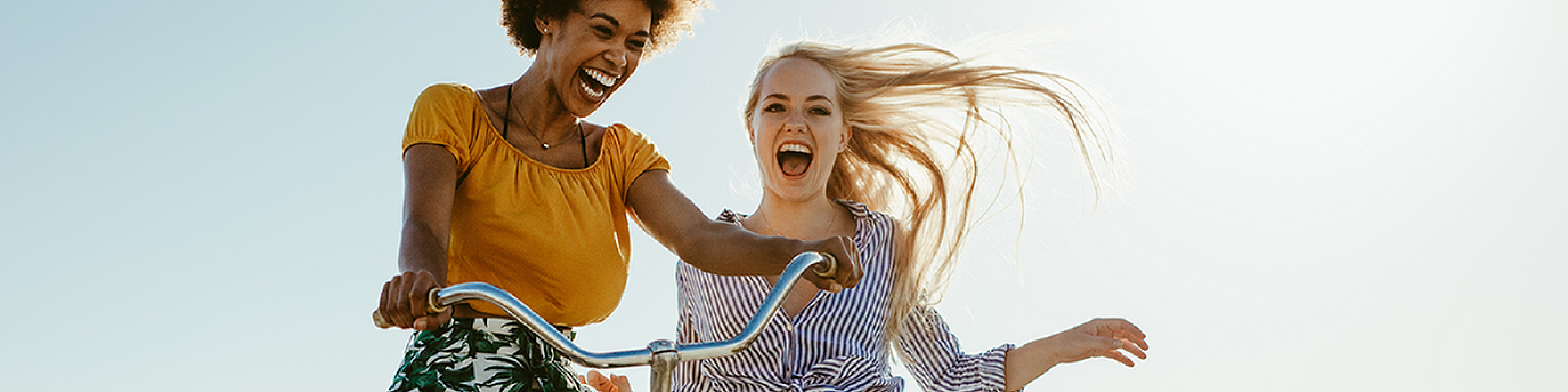 Joyful moment of two friends enjoying a scenic bike ride on a sunny boardwalk by the sea, exuding happiness and freedom.