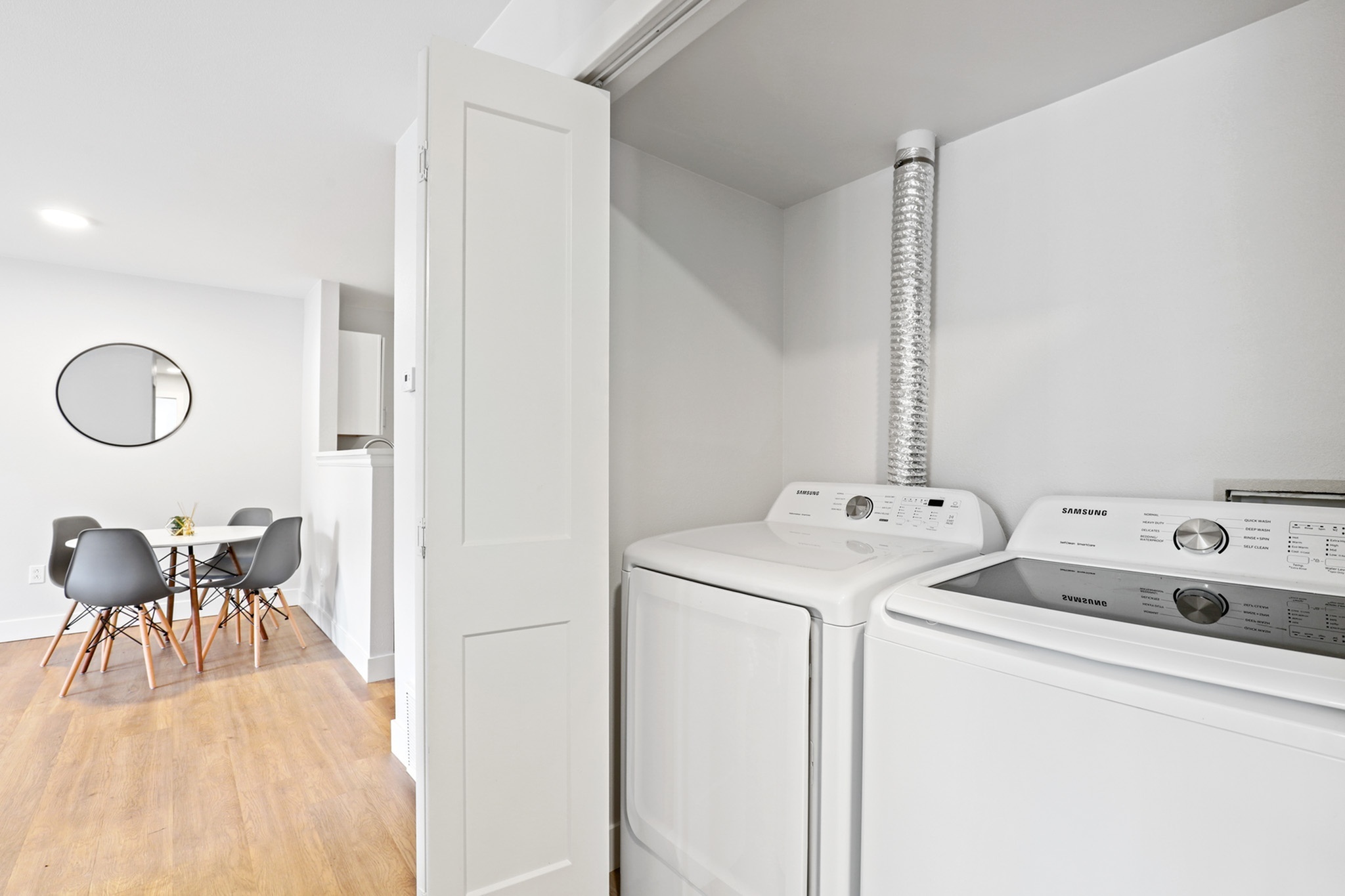 Chic apartment laundry area with modern washer and dryer, spacious layout with a stylish dining area featuring contemporary chairs and a sleek round mirror.