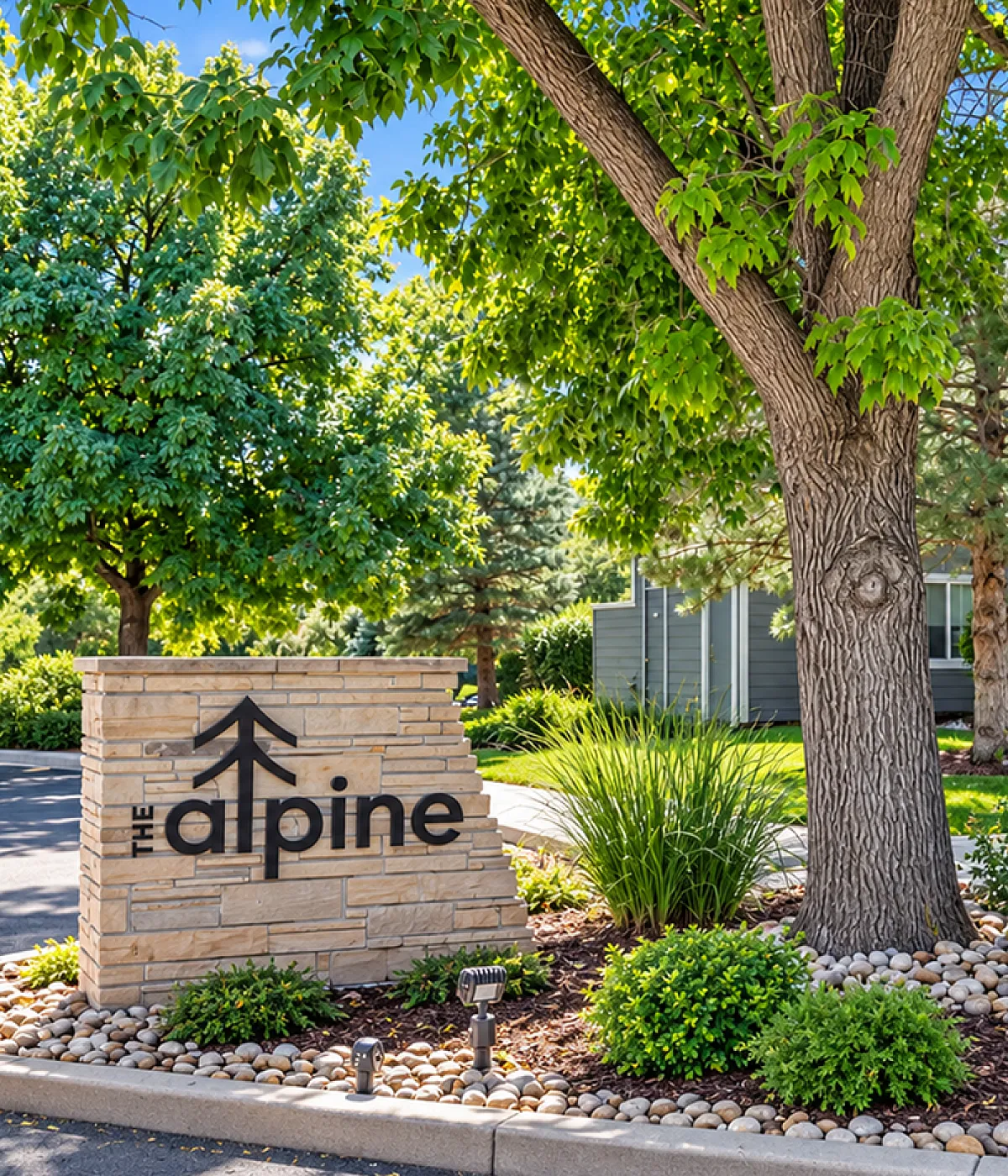 Charming exterior view of The Alpine apartments surrounded by lush greenery and vibrant landscaping.