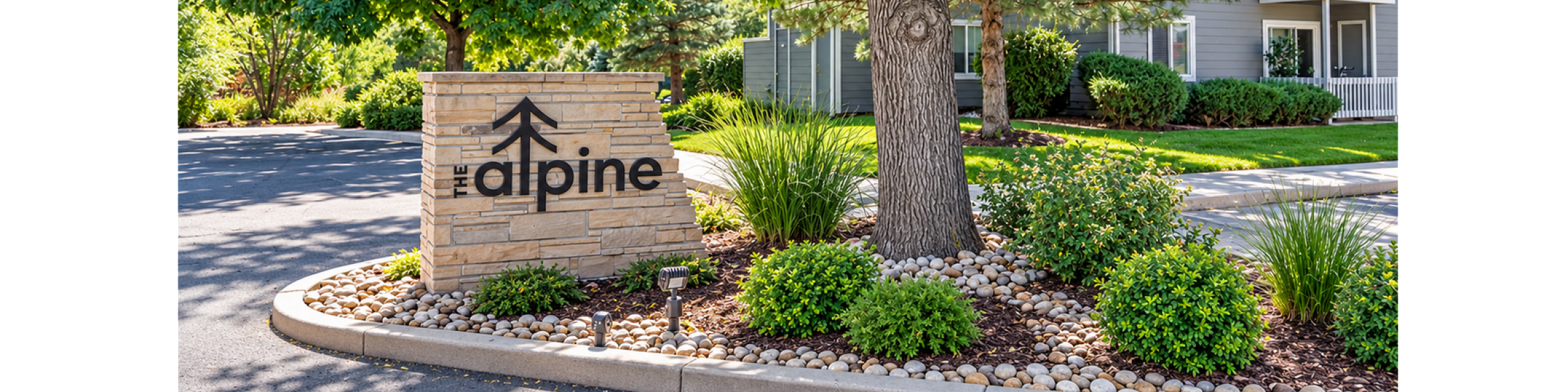 Charming entrance to The Alpine apartments, surrounded by lush greenery and elegant landscaping.