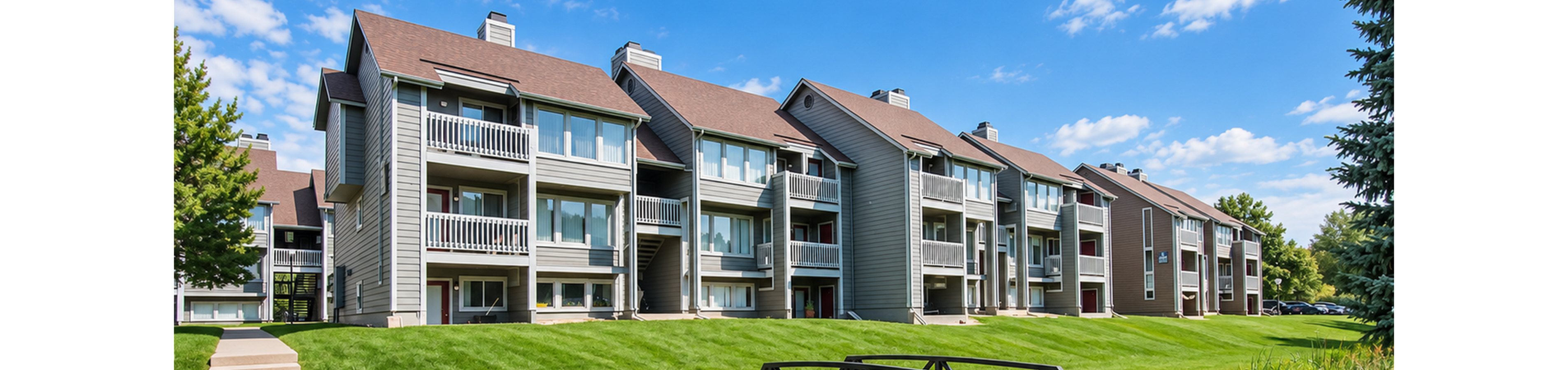 Charming apartment complex with spacious balconies, lush greenery, and a scenic footbridge over a serene stream.