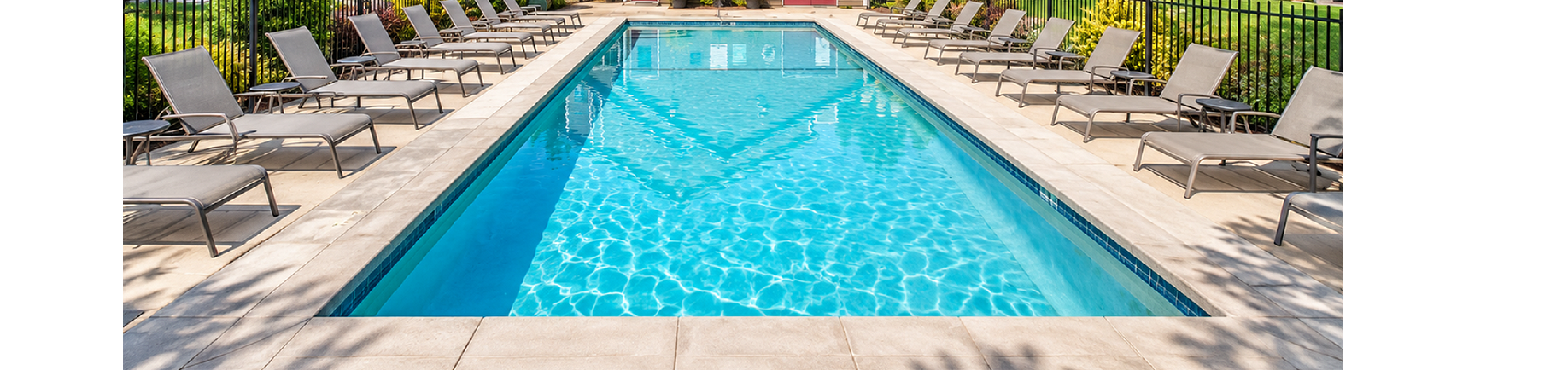 Inviting swimming pool area with sun loungers, surrounded by lush greenery and modern apartments under a bright blue sky.