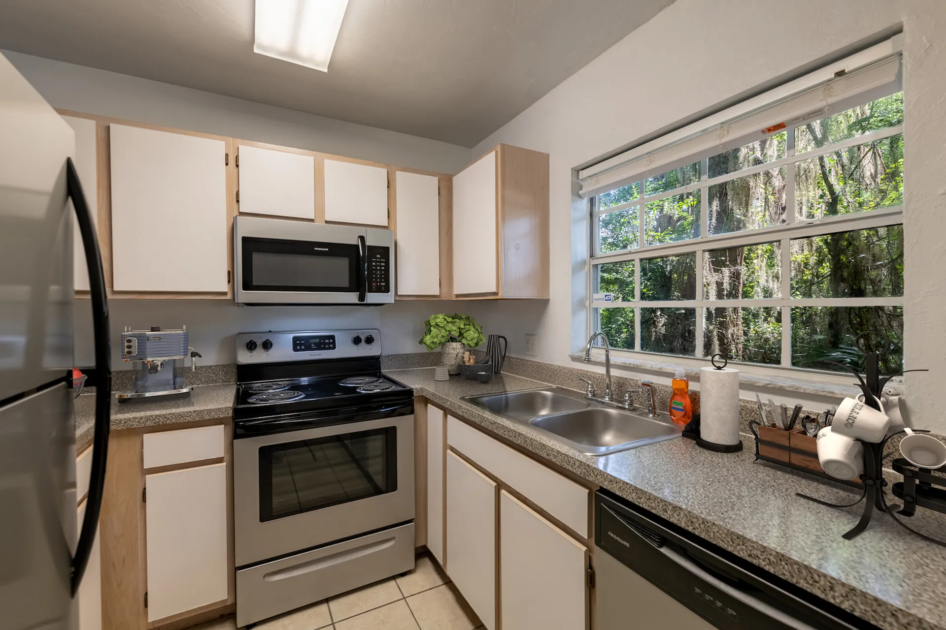 Tiled floor kitchen with white and exposed cabinets, stainless steel appliances and granite like countertops.