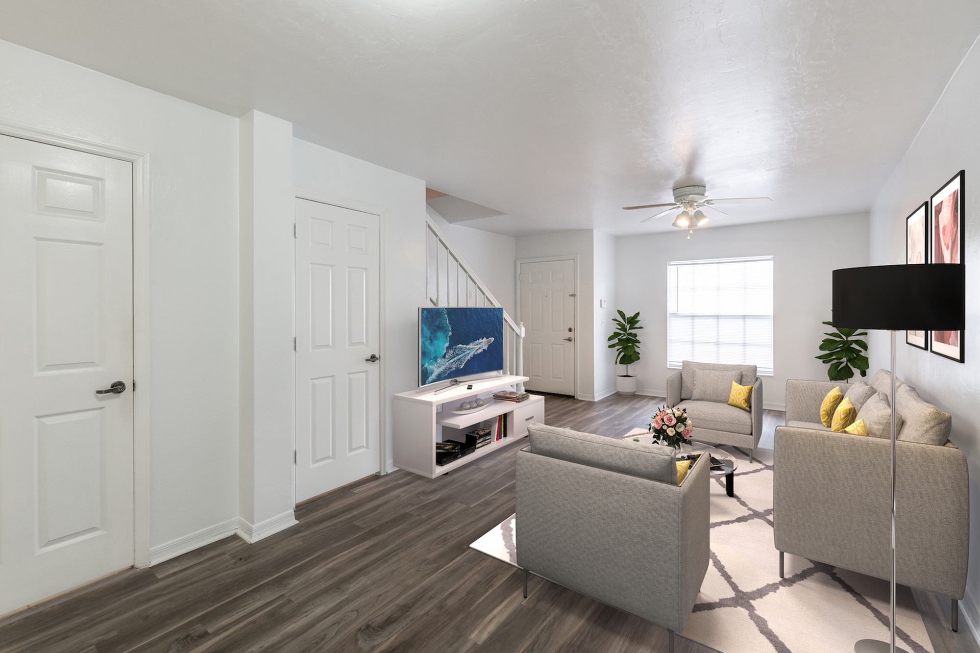 Living area with hardwood floors, white walls, modern furniture, and a staircase. There are two chairs, 1 couch, coffee table and a white media center.