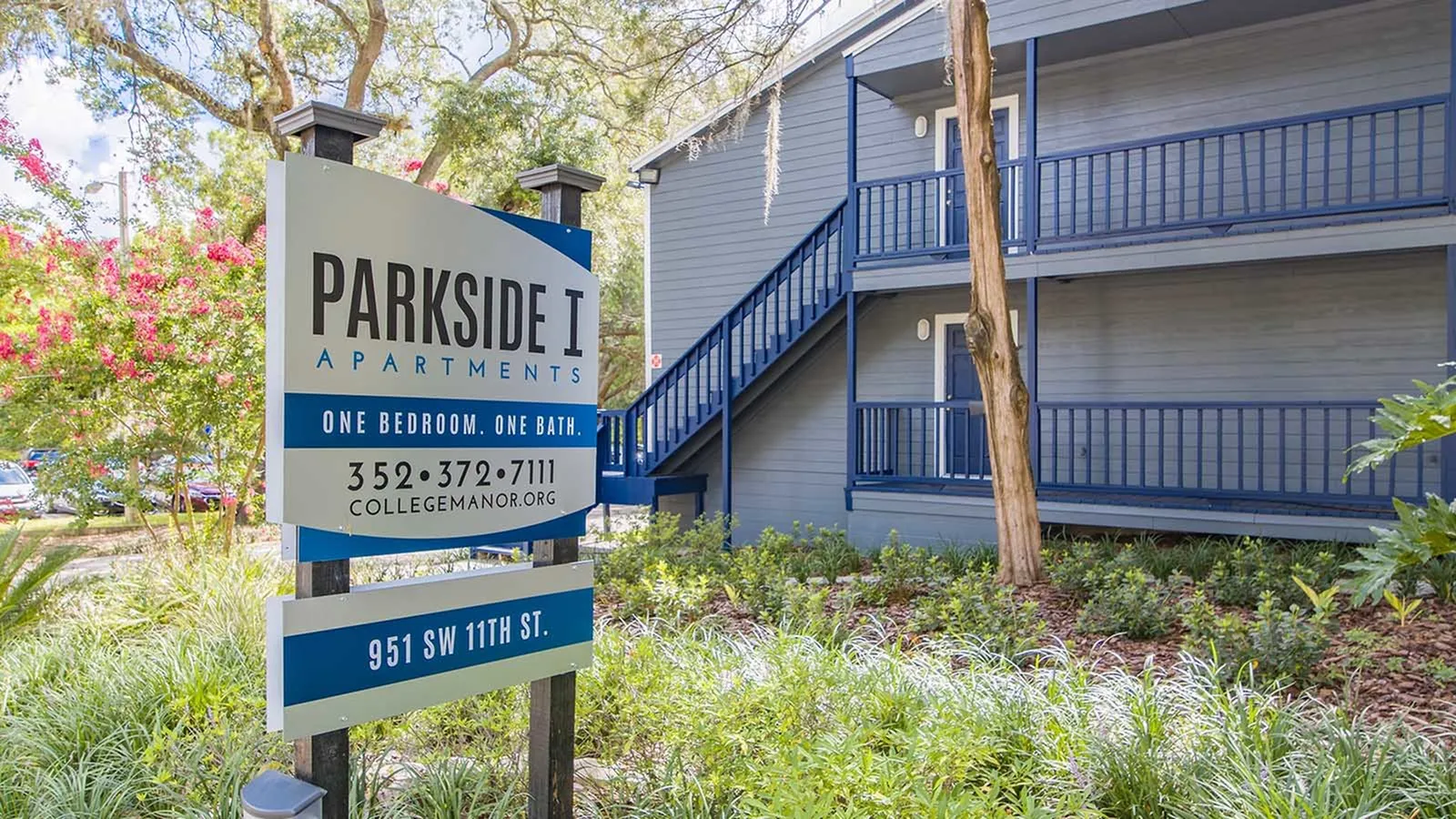 Parkside I (part of College Manor) monument sign surrounded by landscaping and an apartment building in the background.
