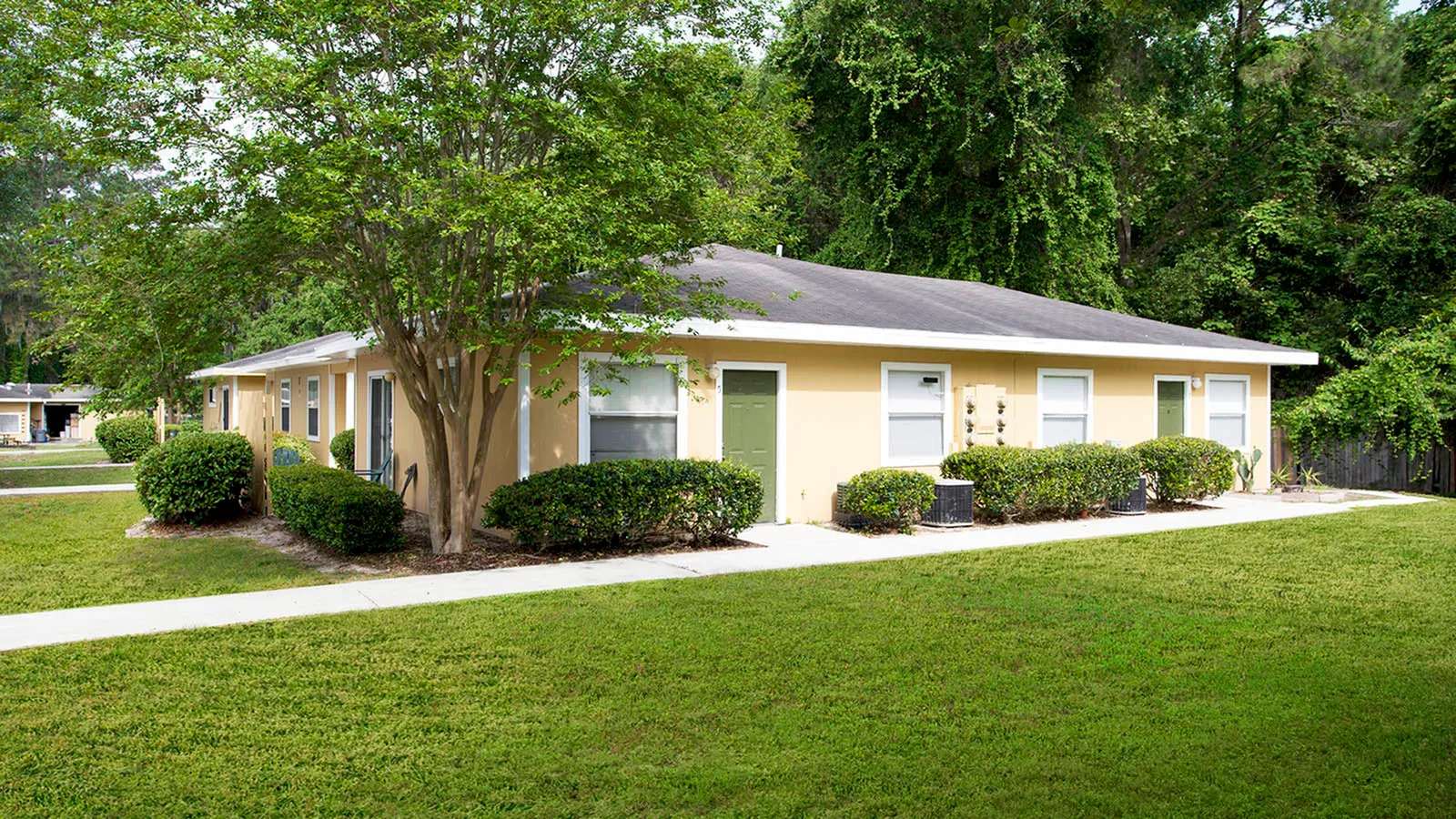 Apartment building painted yellow with lush green grass and lots of trees.
