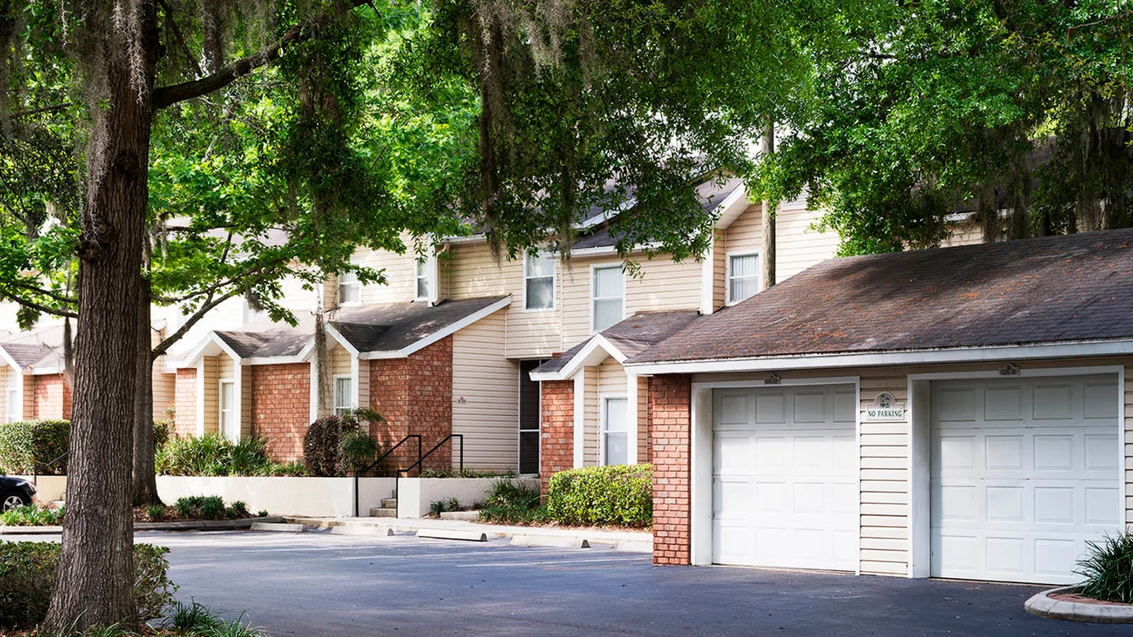Front of apartment buildings including two garage doors and a large tree on the right.