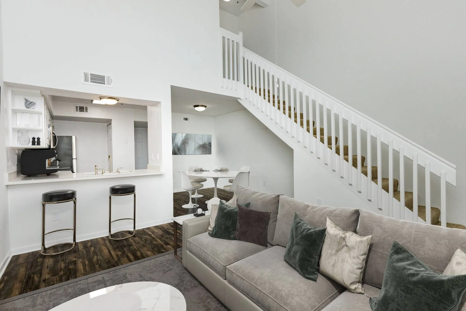 Living area looking into kitchen, breakfast bar with two stools, and a stairway on the right.