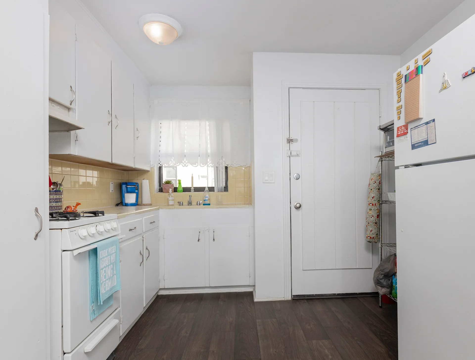 Kitchen with beige tile backsplash, dark hardwood floors and white cabinetry.