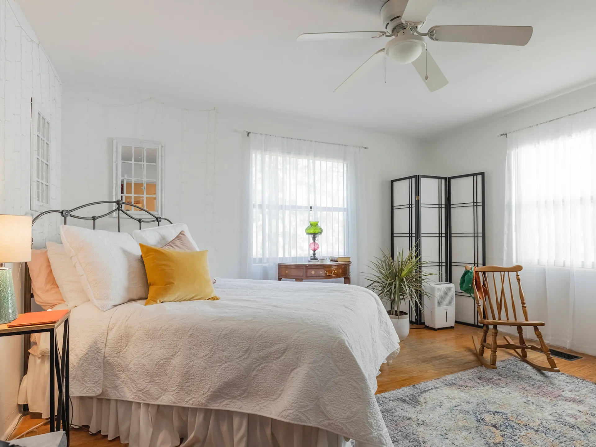 Bedroom with ceiling fan, two windows, hardwood floors, bed, end table with lamp, and area rug.