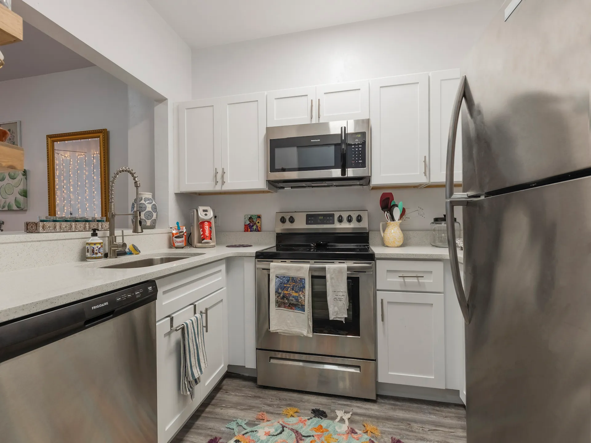 Kitchen with quartz countertops, hardwood floors, white cabinets, stainless steel appliances, and a passthrough