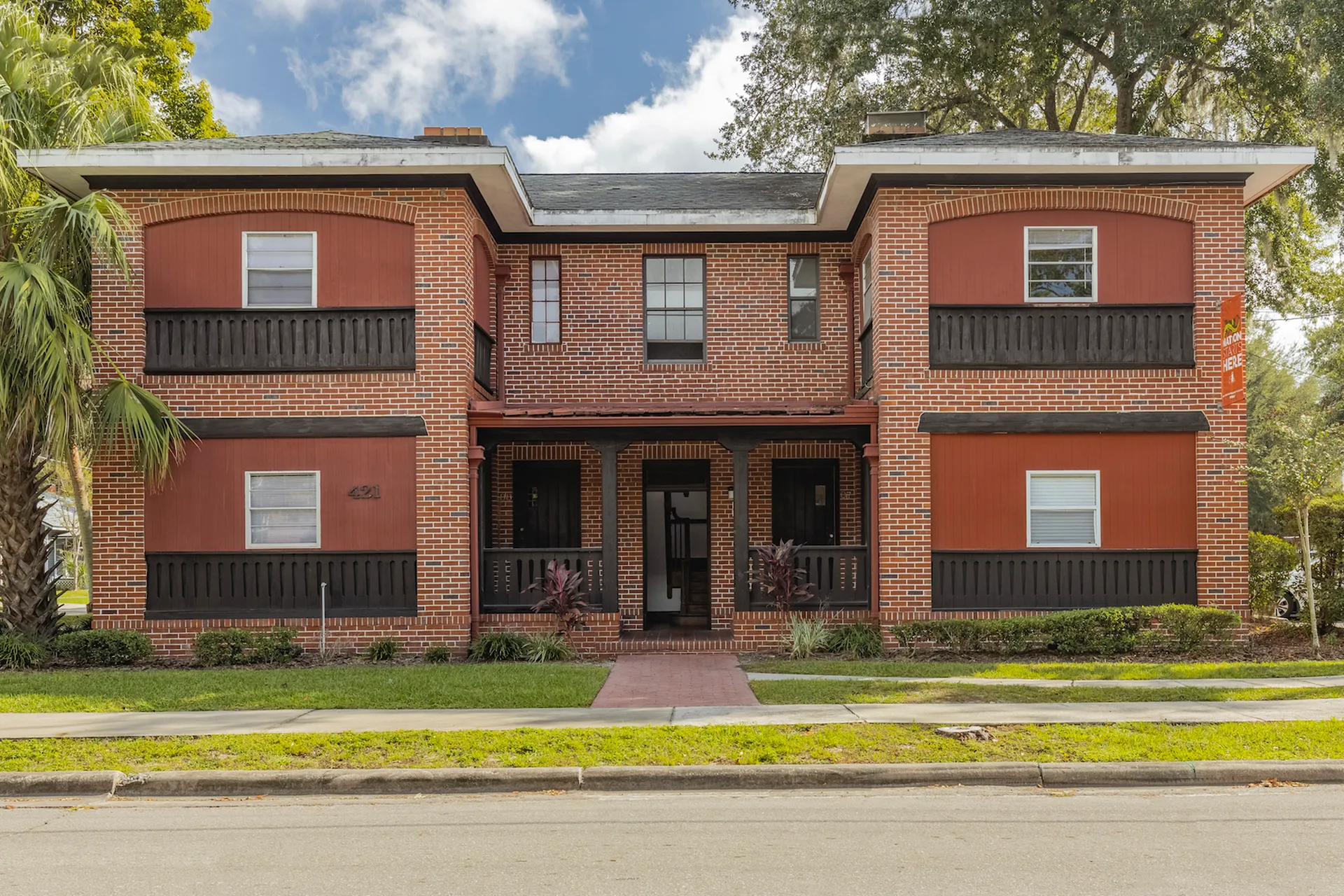 Exterior of the two story 421 Bristol building. There is a sidewalk that leads up to the front steps, and the building itself has exposed red brick walls.