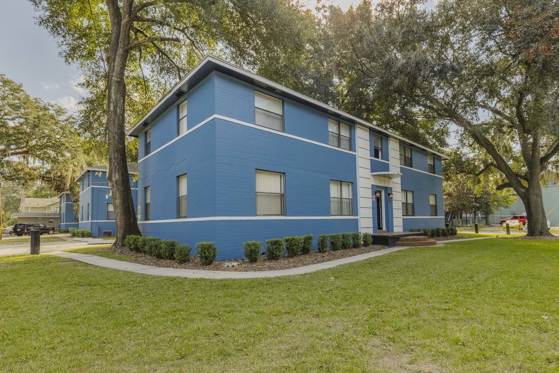 Exterior of the two story Midtown Manor building. The building is blue with white stripes, and there is a sidewalk that wraps around the building.