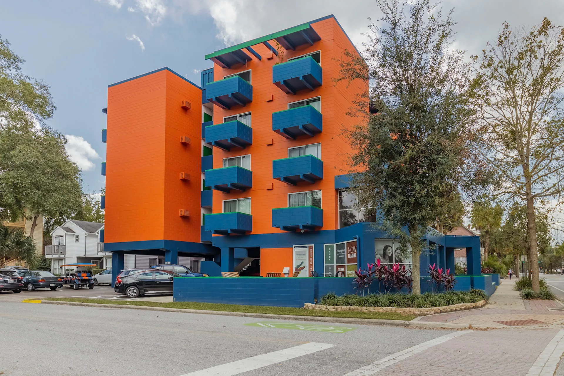 Exterior of the Orange and Blue building. There is a road in front that leads to covered parking and a sidewalk that wraps around the building.
