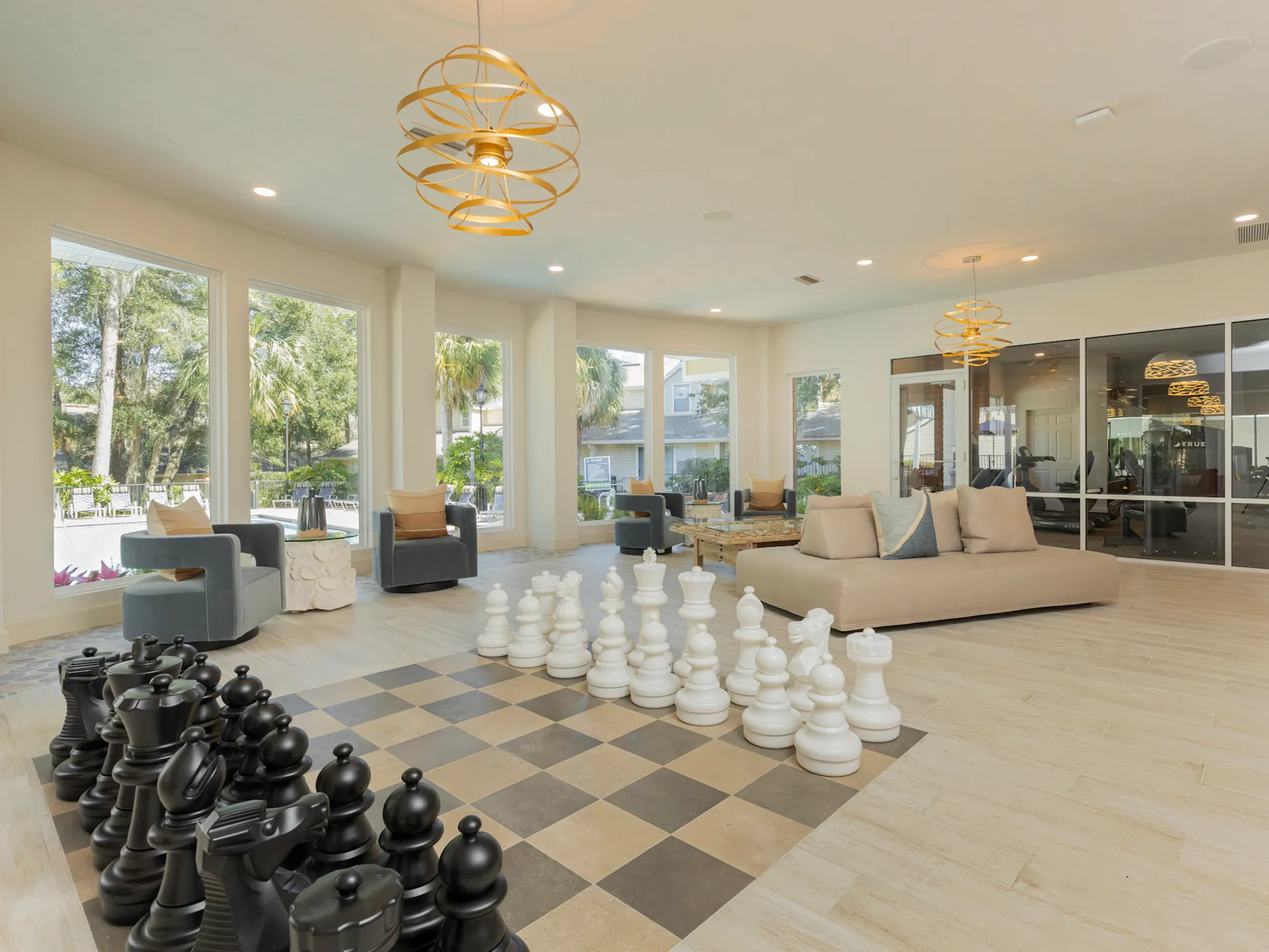 Community clubhouse with large windows facing the community pool, life-size chess, and the community gym in the background.