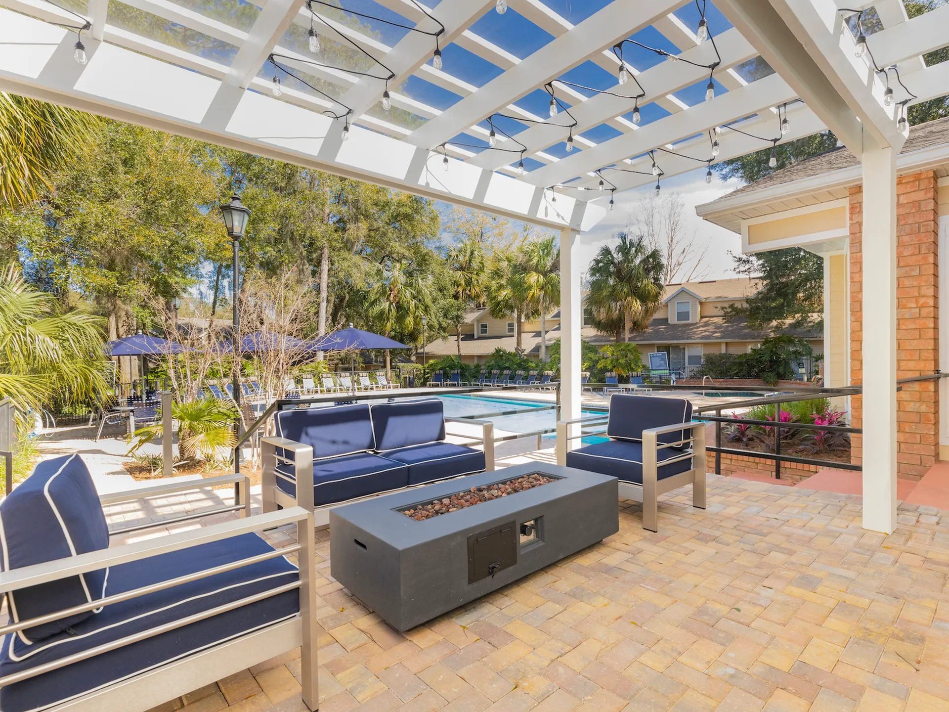 Patio seating under a pergola next to the community pool. There is a fire pit in the center of the patio set.