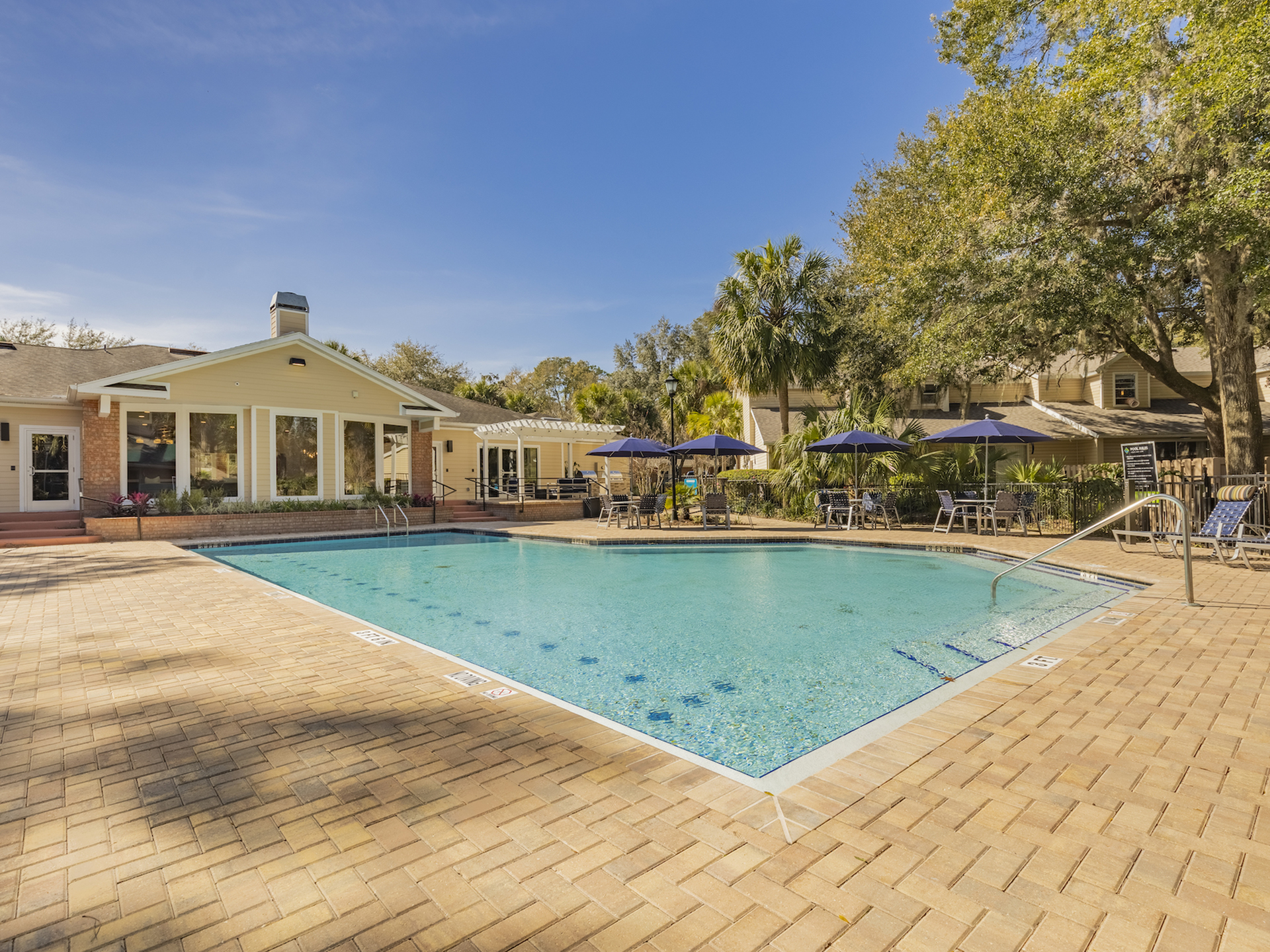 Community pool with traditional seating as well as lounge seating, a barbecue area, as well as the clubhouse in the background.