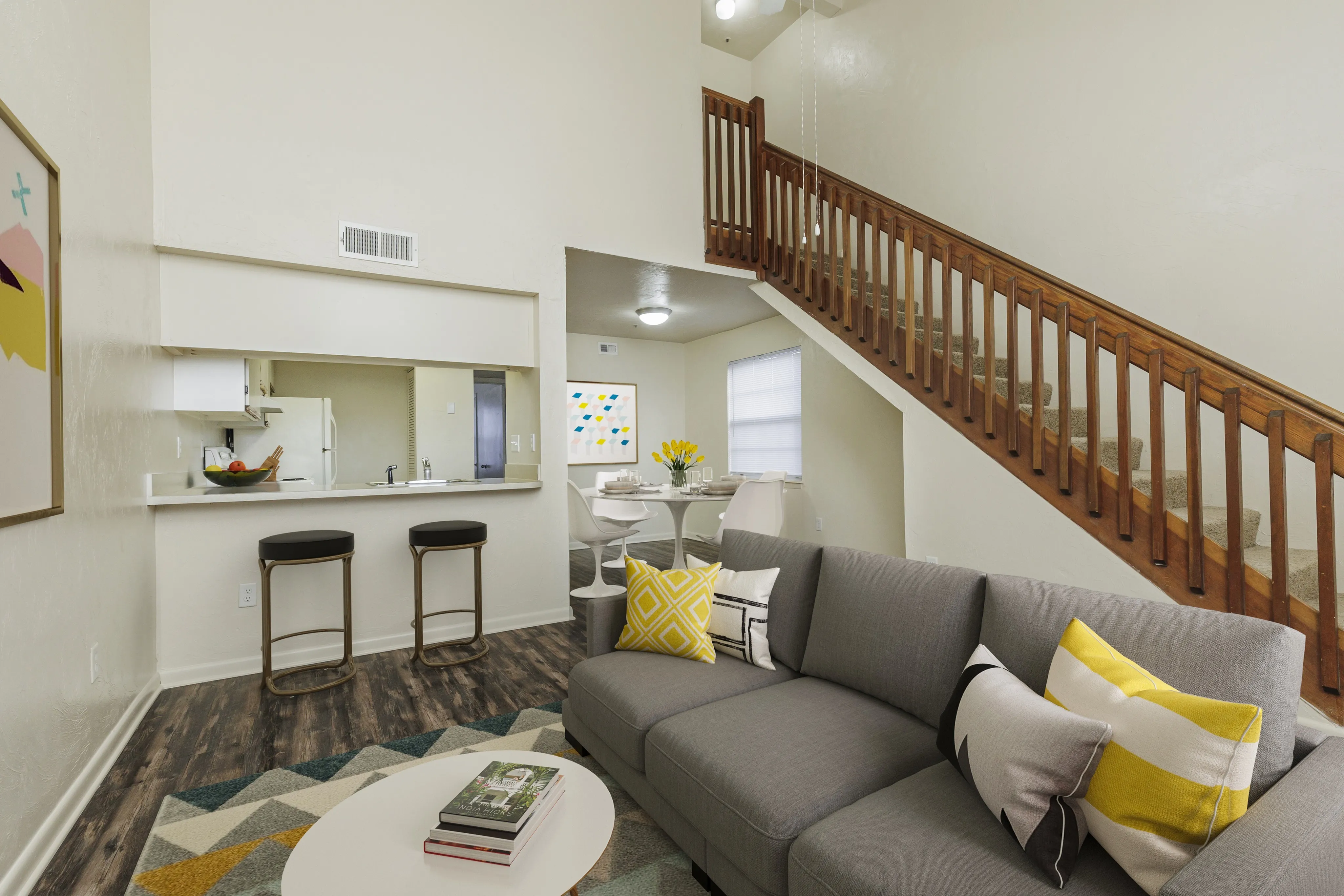 Living area looking into kitchen, breakfast bar with two stools, and a stairway on the right.
