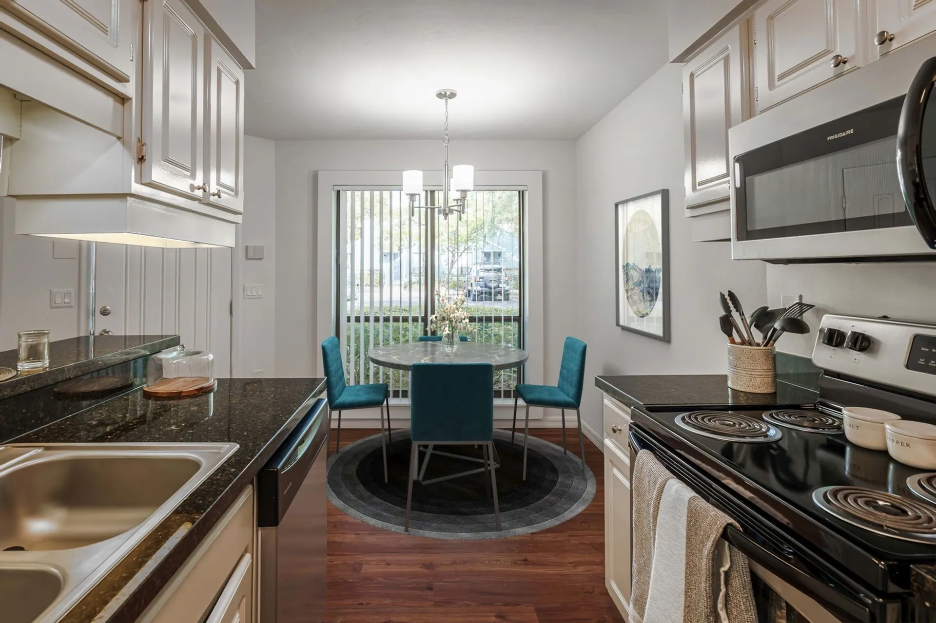 Kitchen with black granite countertop, white classic cabinets, and stainless steel over overlooking dining area with full size window