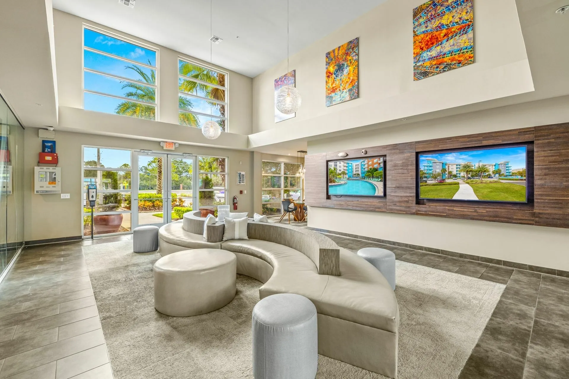 Community clubhouse with modern couch loaded with pillows.  Leasing offices behind glass walls in background.