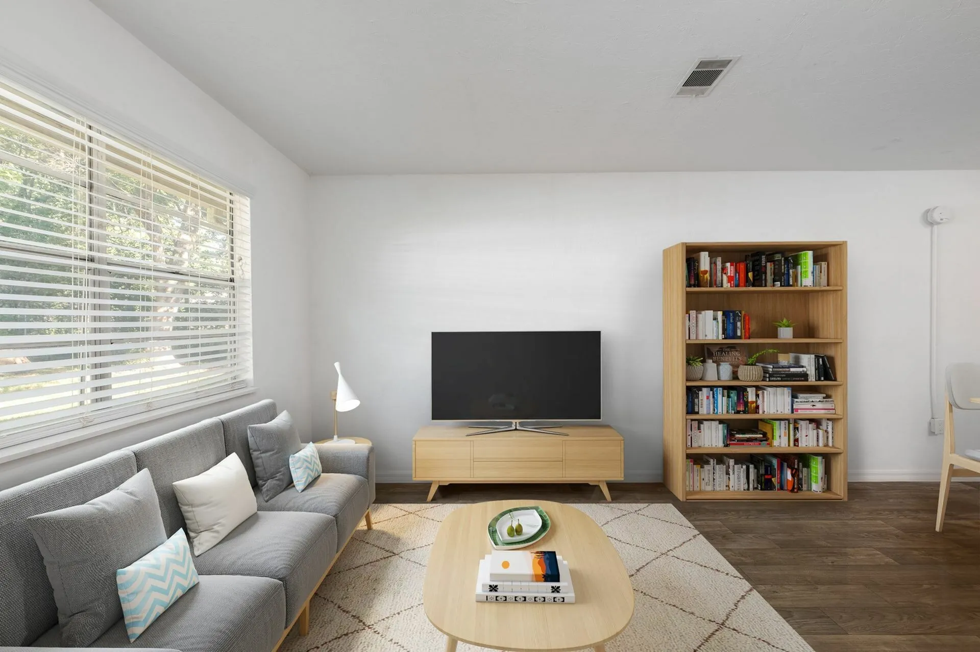 Living room with hardwood floors, contemporary furniture, wall mounted television and wall art. You can see a large window in the background as well as the entrance to the apartment.