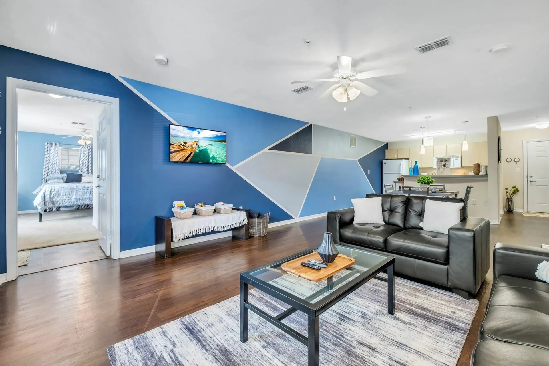 Living area with hardwood floors, white and blue accent wall, and a large window.