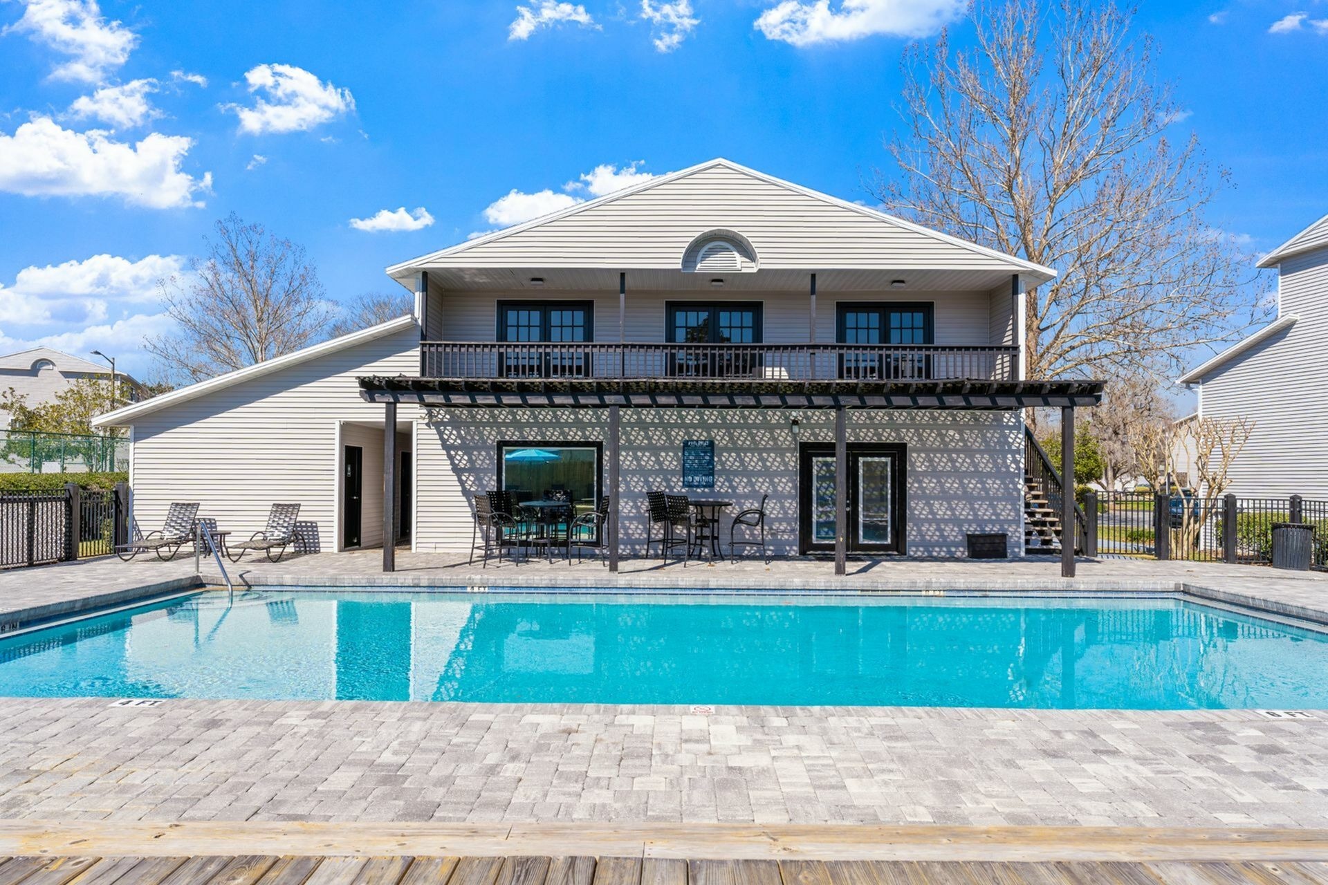 Community pool surrounded with pavers and clubhouse in the background.