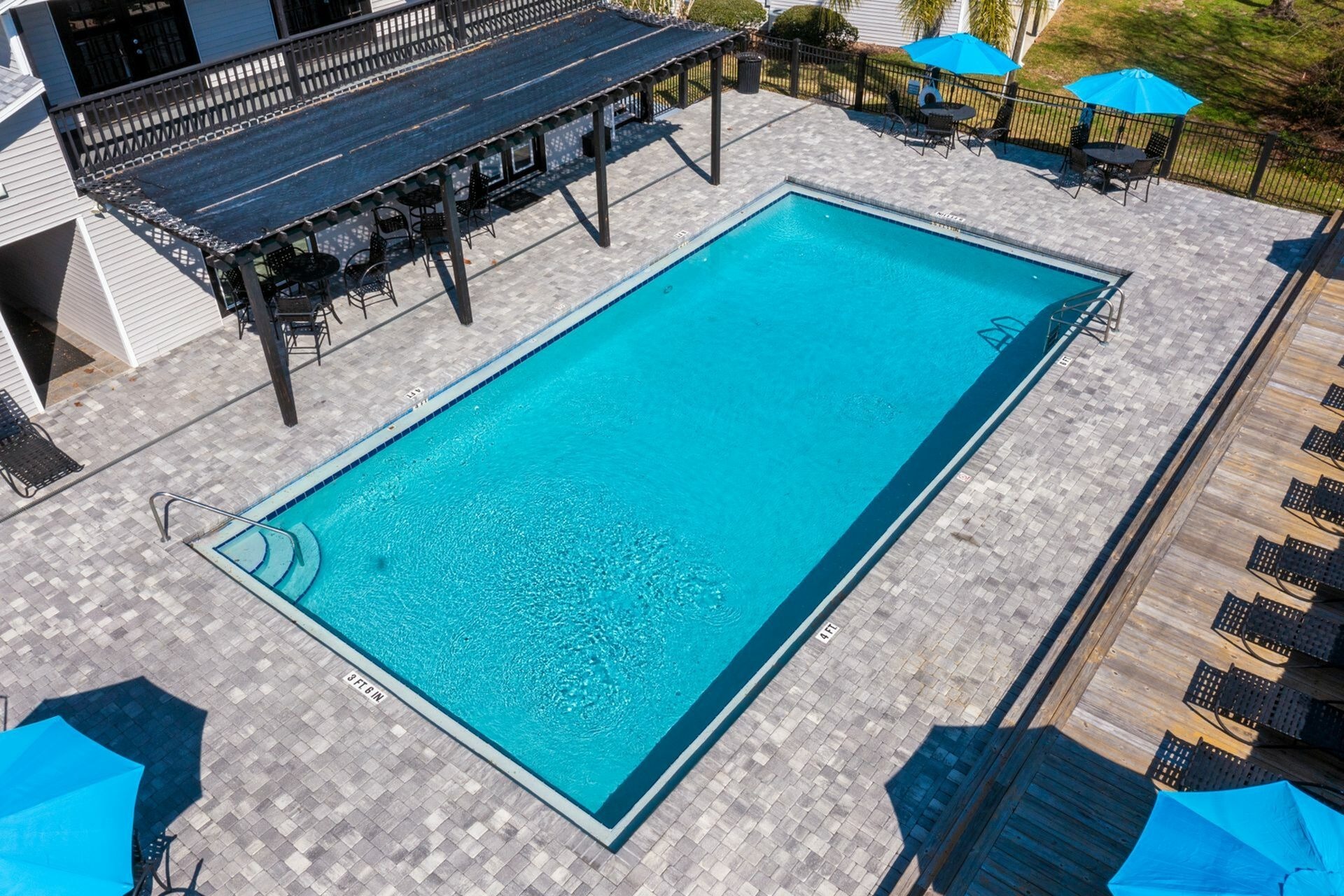 Community pool surrounded with pavers and clubhouse in the background.