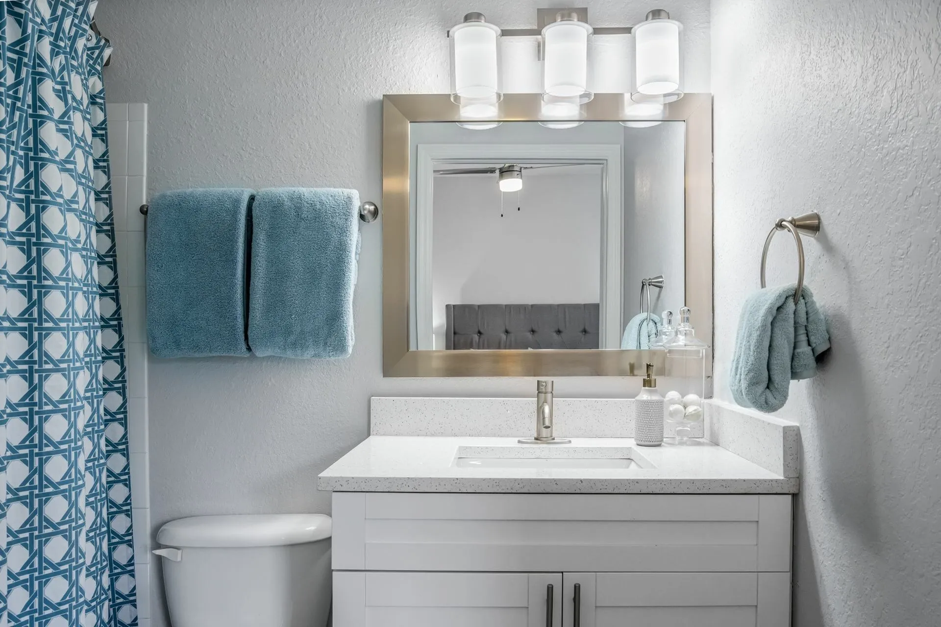 Bathroom with quartz countertop, gold framed mirror and blue towels, hand towels and shower curtain