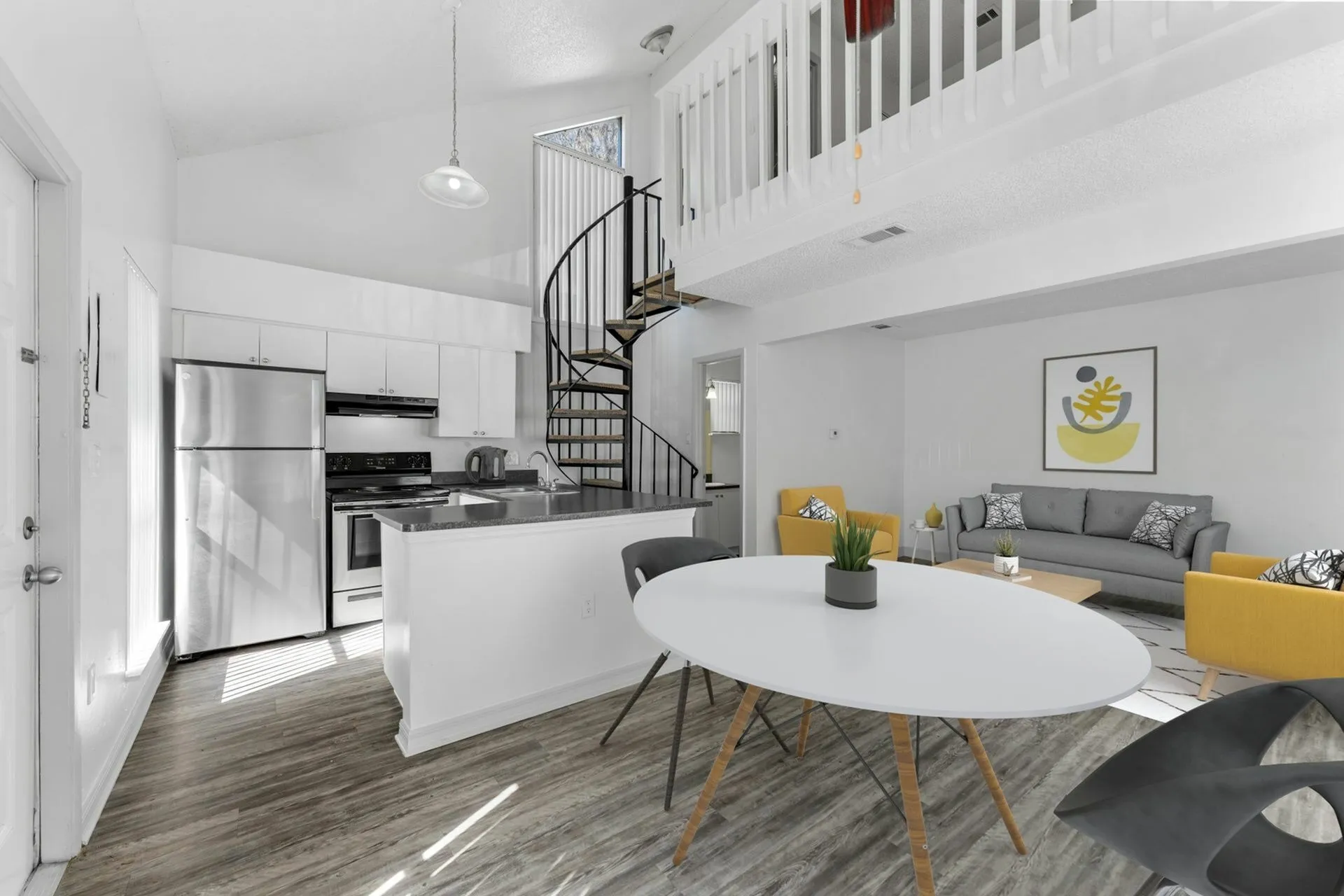 Close up of the open concept kitchen with white appliances, wood style countertops, white cabinets and a spiral staircase in the background.