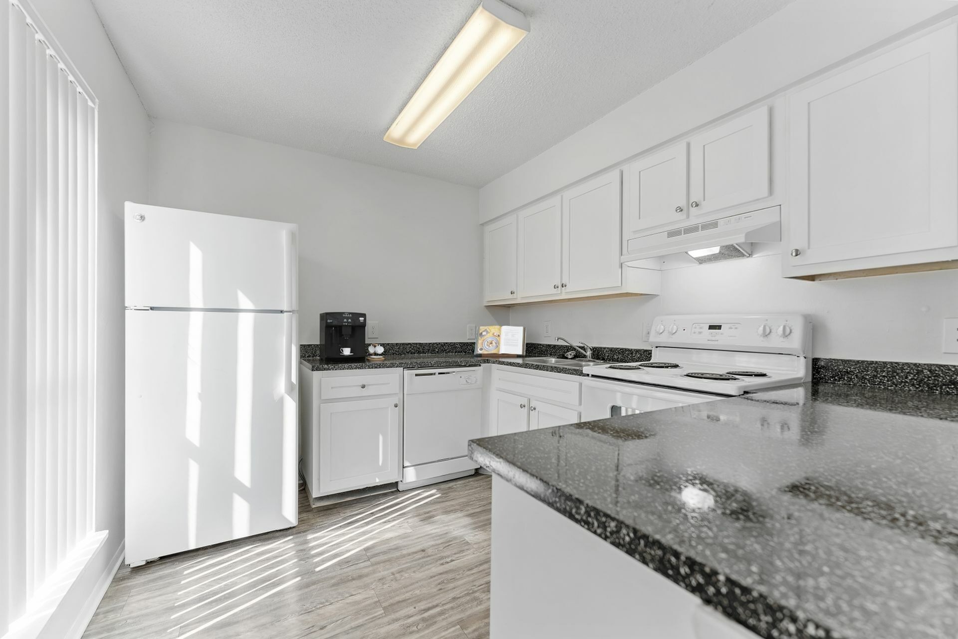 Kitchen with hardwood floors, grey countertops, black appliances, and white cabinets.