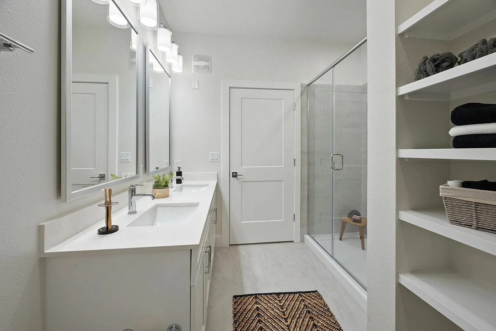 Modern bathroom featuring a dual-sink vanity, spacious glass-enclosed shower, and built-in shelving.