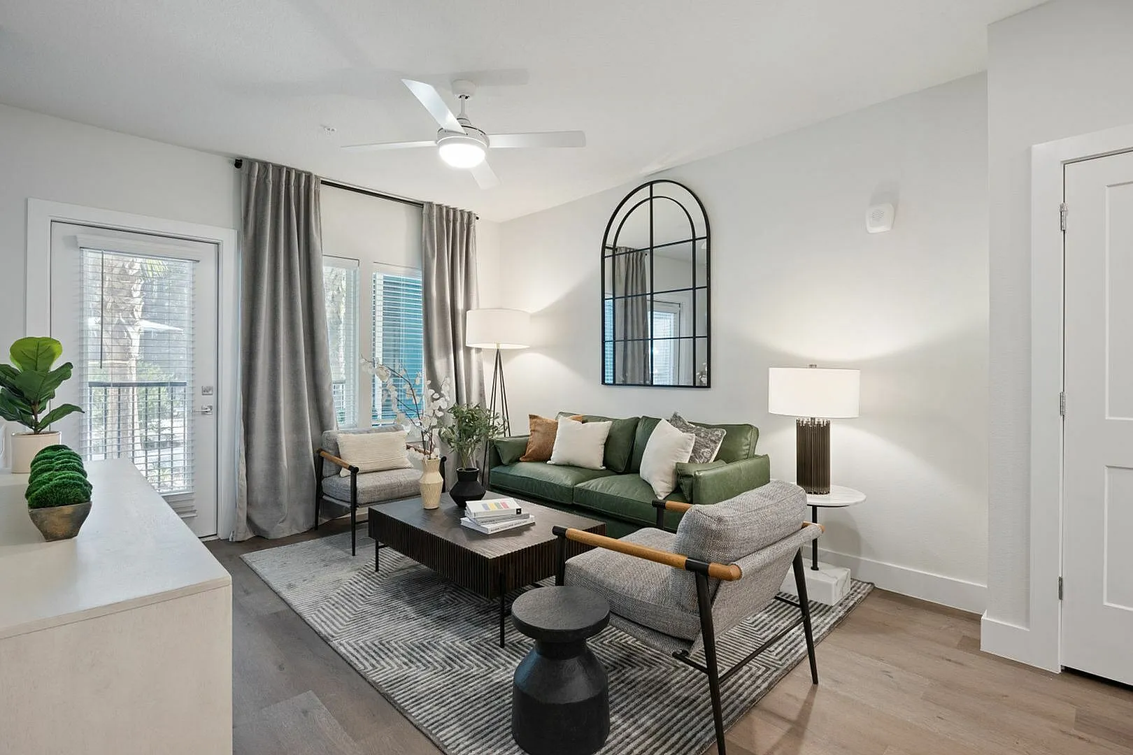 Chic living room with green sofa, modern decor, and floor-to-ceiling windows.